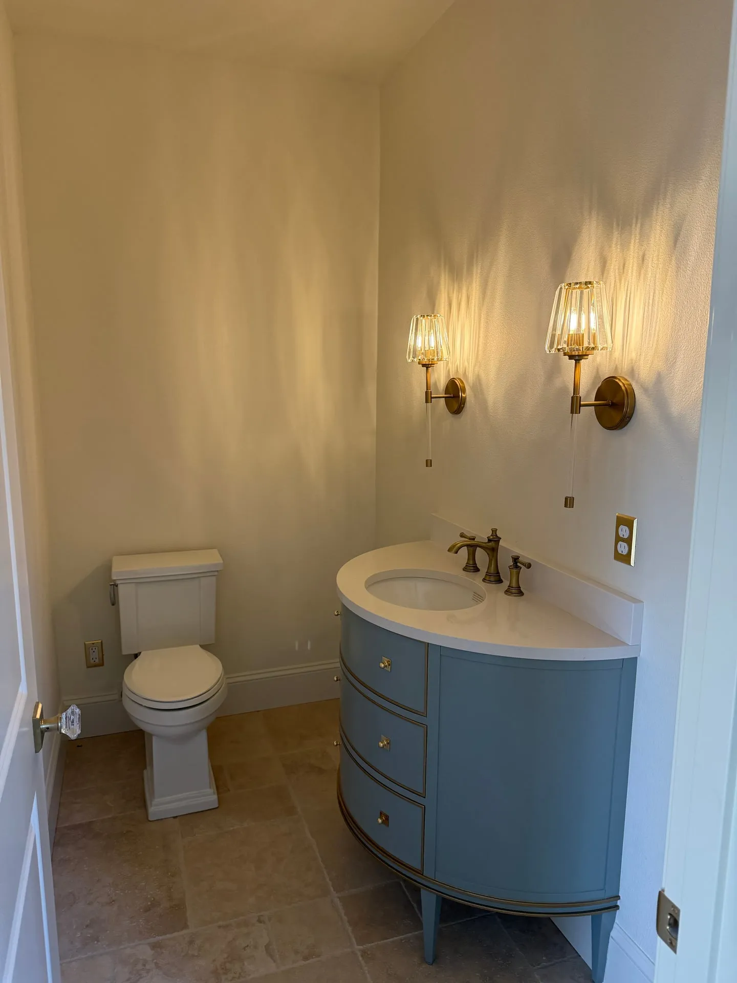 Paired glass and brass sconces flanking a bathroom mirror position in a custom home in Ridgefield WA, above a blue vanity with a marble top