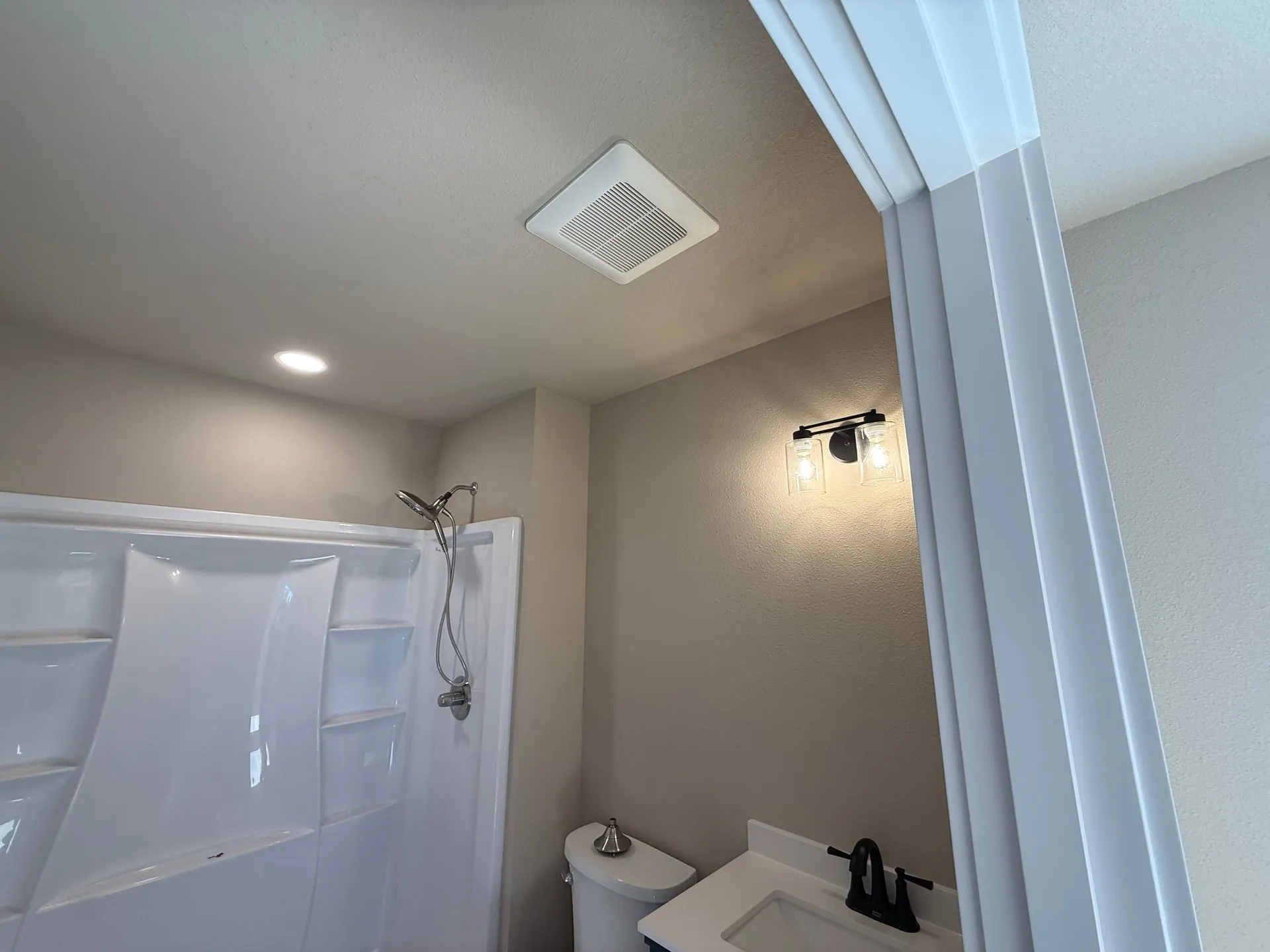 Finished bathroom in a new shop building in Hazel Dell, Vancouver WA with a Panasonic exhaust fan grille in the ceiling, a vanity light and a walk-in shower