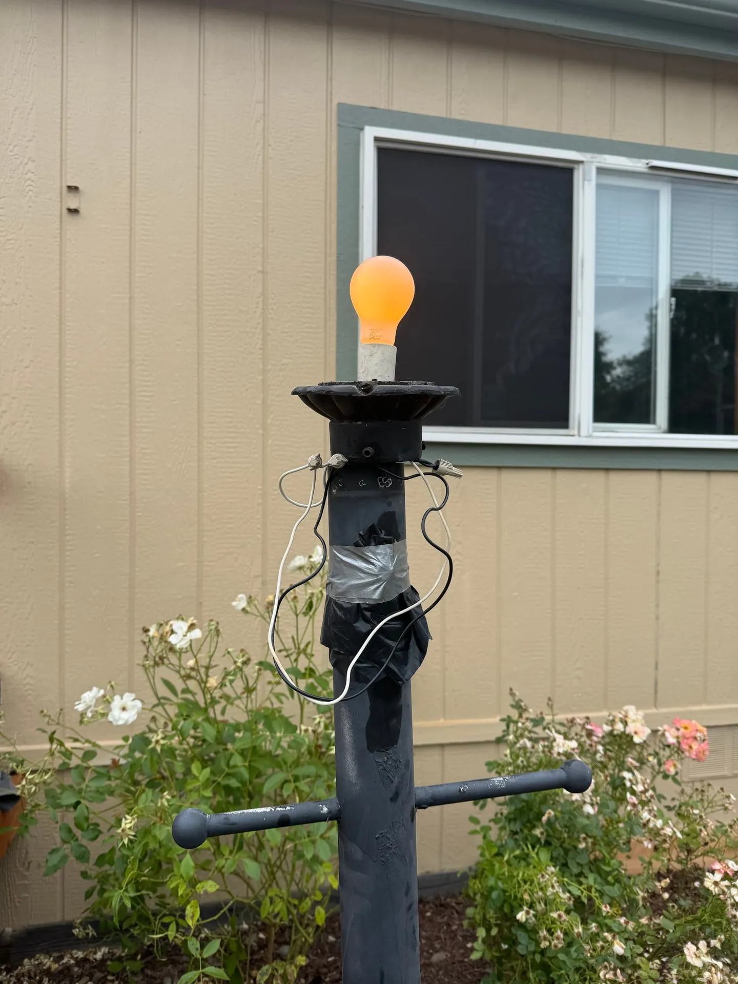 Outdoor post lamp in Orchards, Vancouver WA before repair, reduced to a bare bulb sitting on a broken fixture head with electrical tape wrapped around exposed wiring