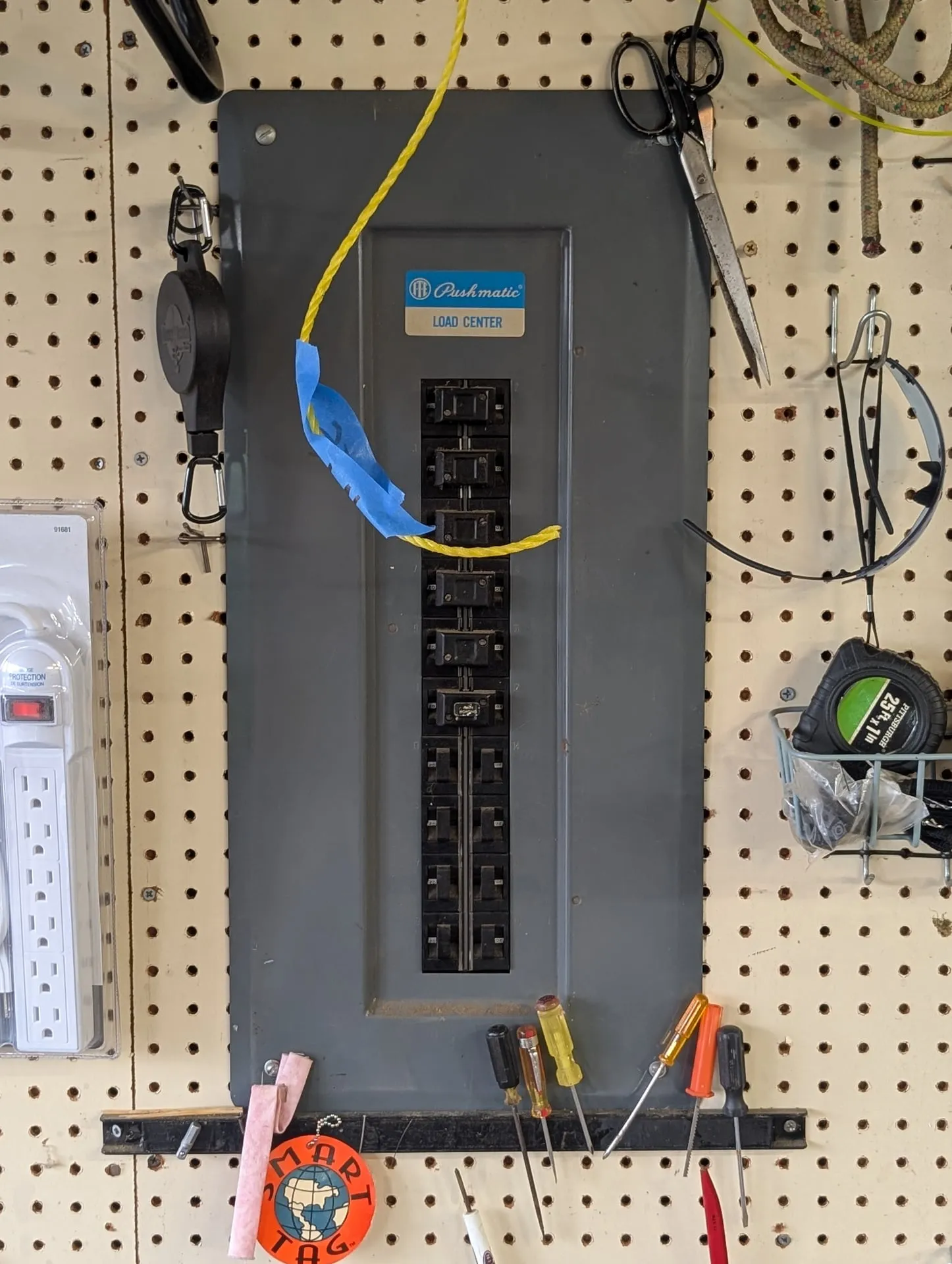 Original ITE Pushmatic load center mounted on a pegboard wall in the garage of a Vancouver WA home before replacement, with the blue Pushmatic badge visible on the dead front