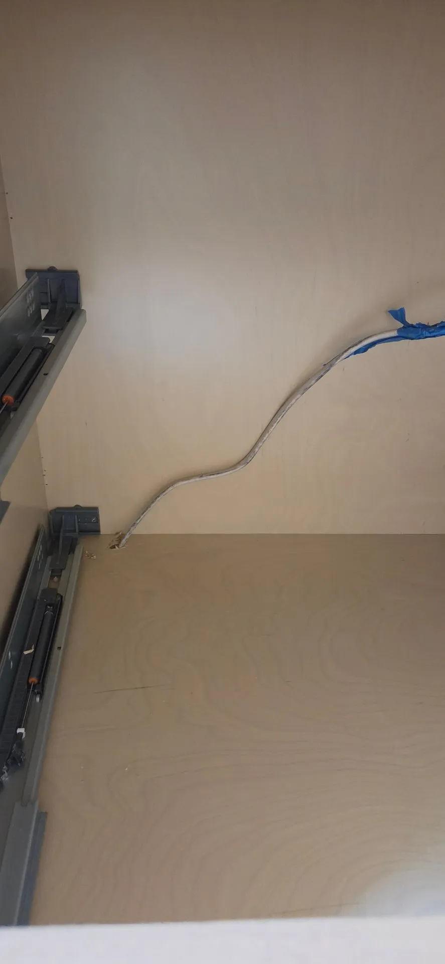 Loose white cable with blue tape on the end coming up through the floor of a drawer base cabinet in a Ridgefield WA kitchen