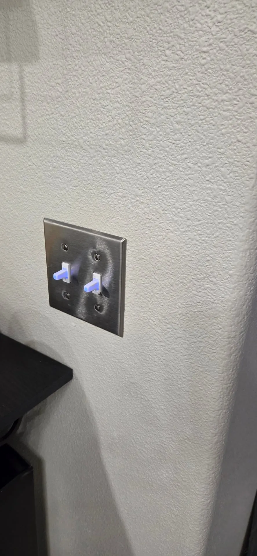 Old two-gang toggle switches with lighted toggles behind a stainless steel cover plate in a Washougal WA home