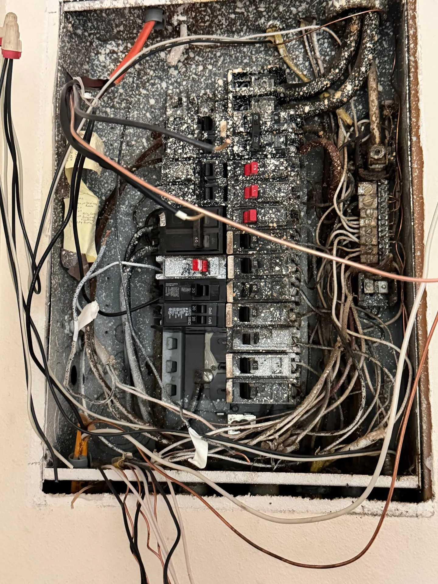 The original 100-amp electrical panel in a pre-1980 Ridgefield WA home before replacement, recessed in a wall and coated in white paint overspray with aged branch circuit conductors crowded around a corroded neutral bar
