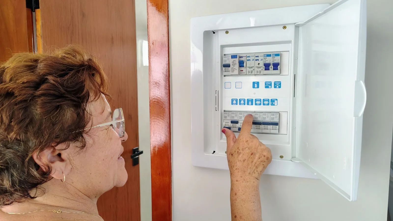 Homeowner reaching toward a row of breakers in an open wall panel to check which one tripped