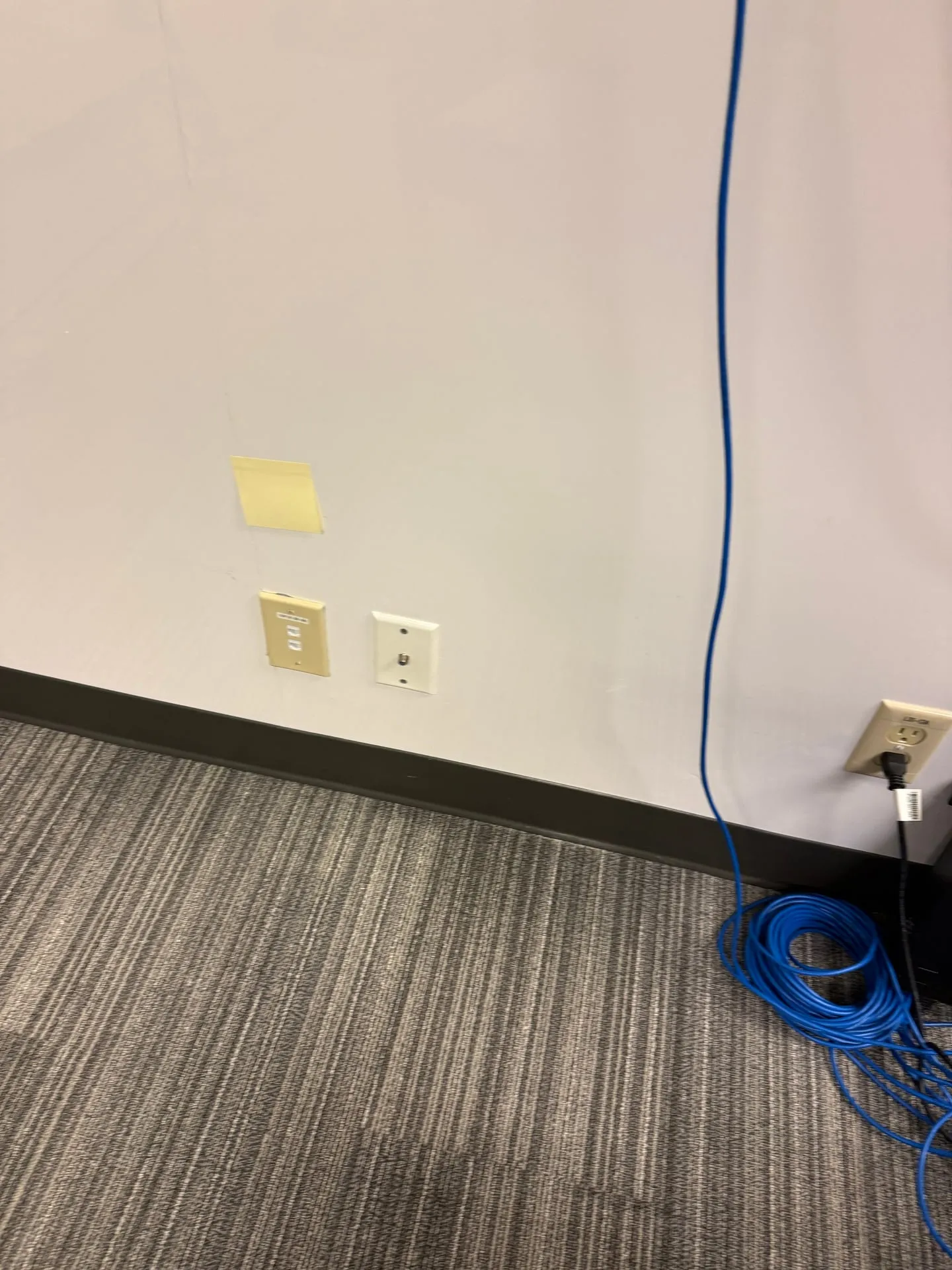 Blue Cat6 cable coiled at the base of an office wall in Vancouver WA below a newly installed data jack, ready to be terminated