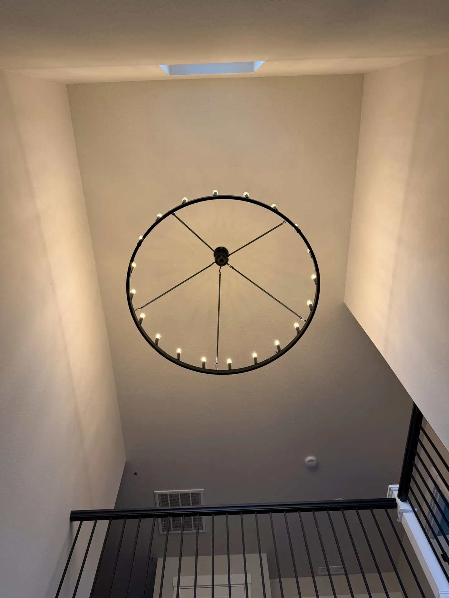 Wagon-wheel chandelier photographed looking straight up from the stairwell landing of a Salmon Creek home in Vancouver WA, showing the full 18-foot ceiling height and the stair railing below