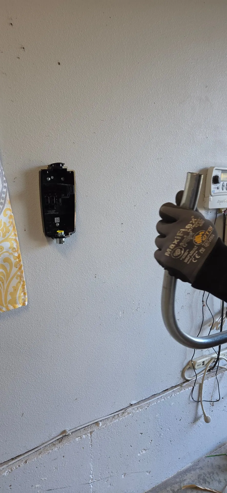 Tesla Wall Connector mounting bracket on a garage wall in Camas WA with the flexible conduit whip being brought to it