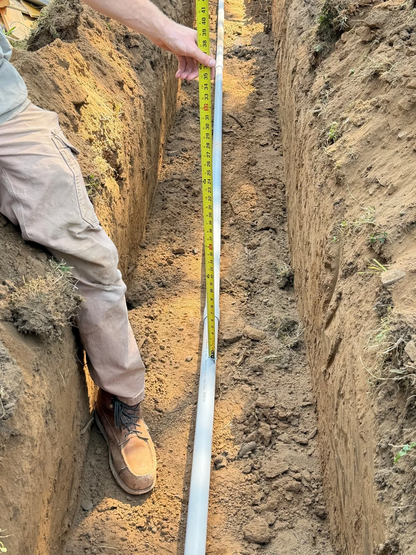 Tape measure held vertically in an open trench next to grey PVC conduit to document burial depth on a Woodland WA sub panel feeder installation