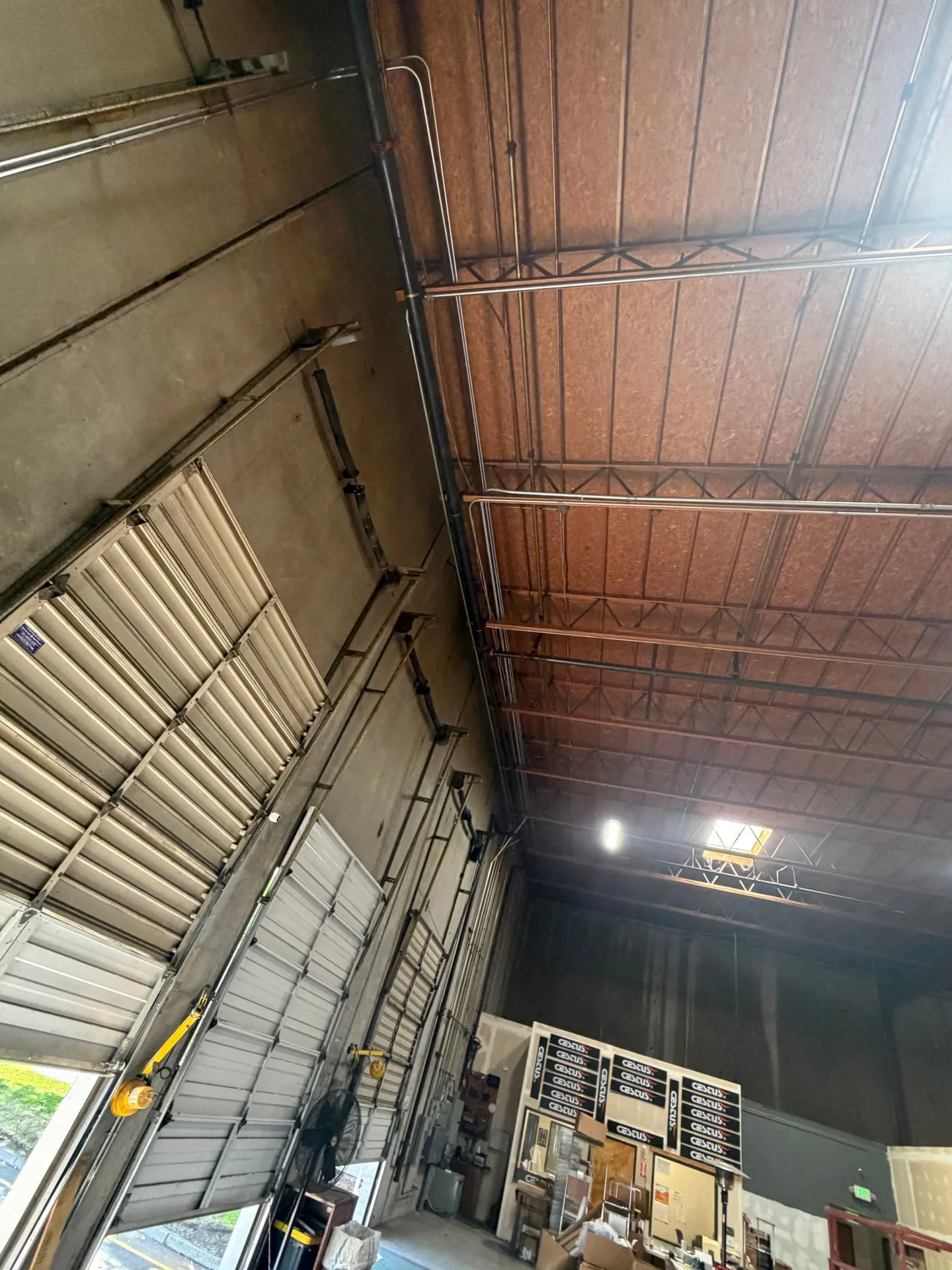 Rigid conduit running along the wall and up under the roof deck of a Vancouver WA warehouse, carrying two new machine circuits above the loading doors
