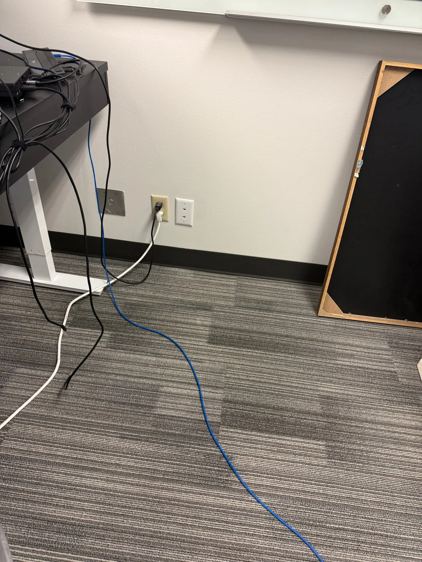 New data jack installed beside an existing power receptacle at a desk position in a Vancouver WA office, with a blue patch lead running to the workstation