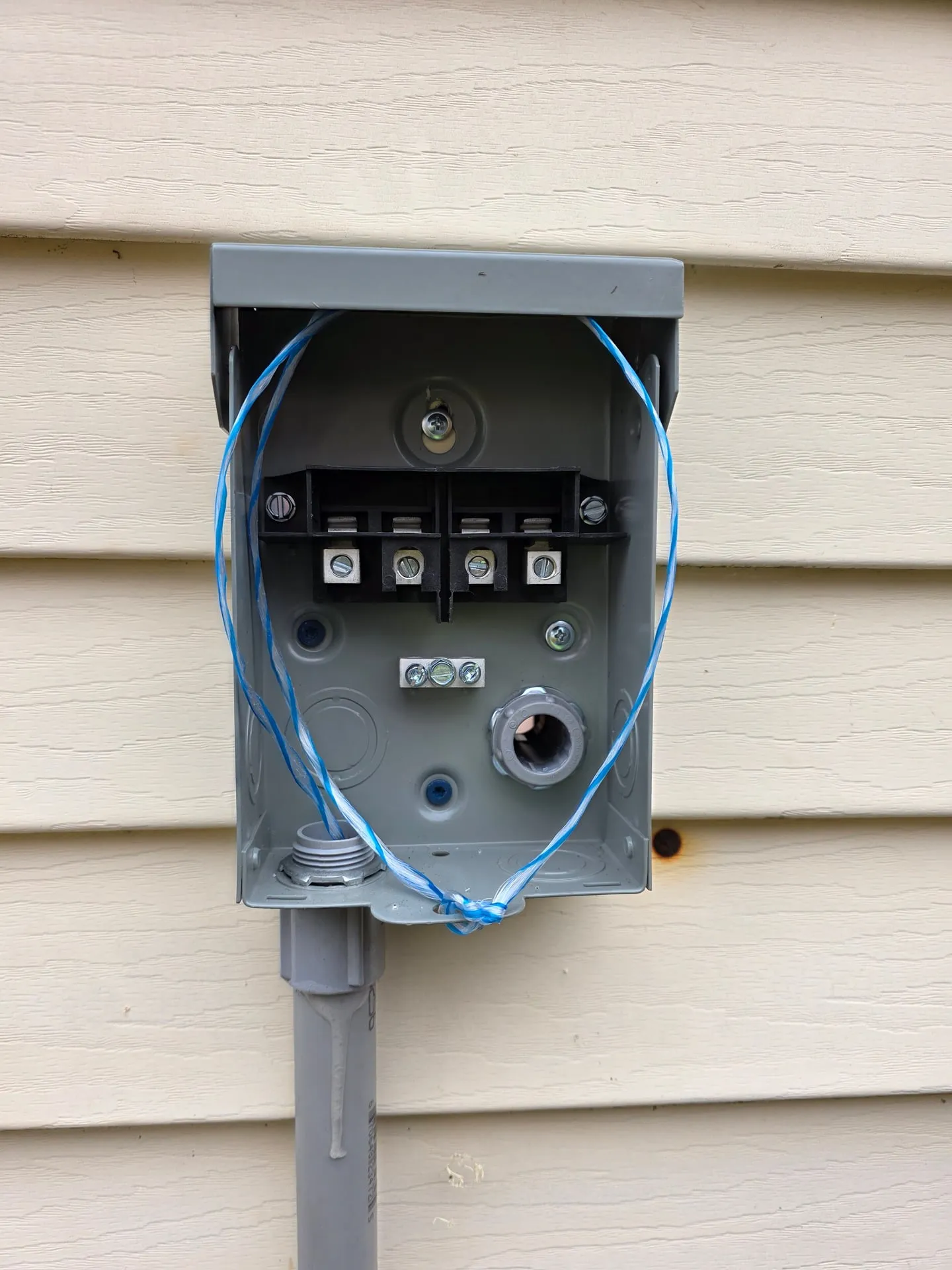 Outdoor disconnect box open on vinyl siding with PVC conduit coming up from the ground at a Washougal WA home