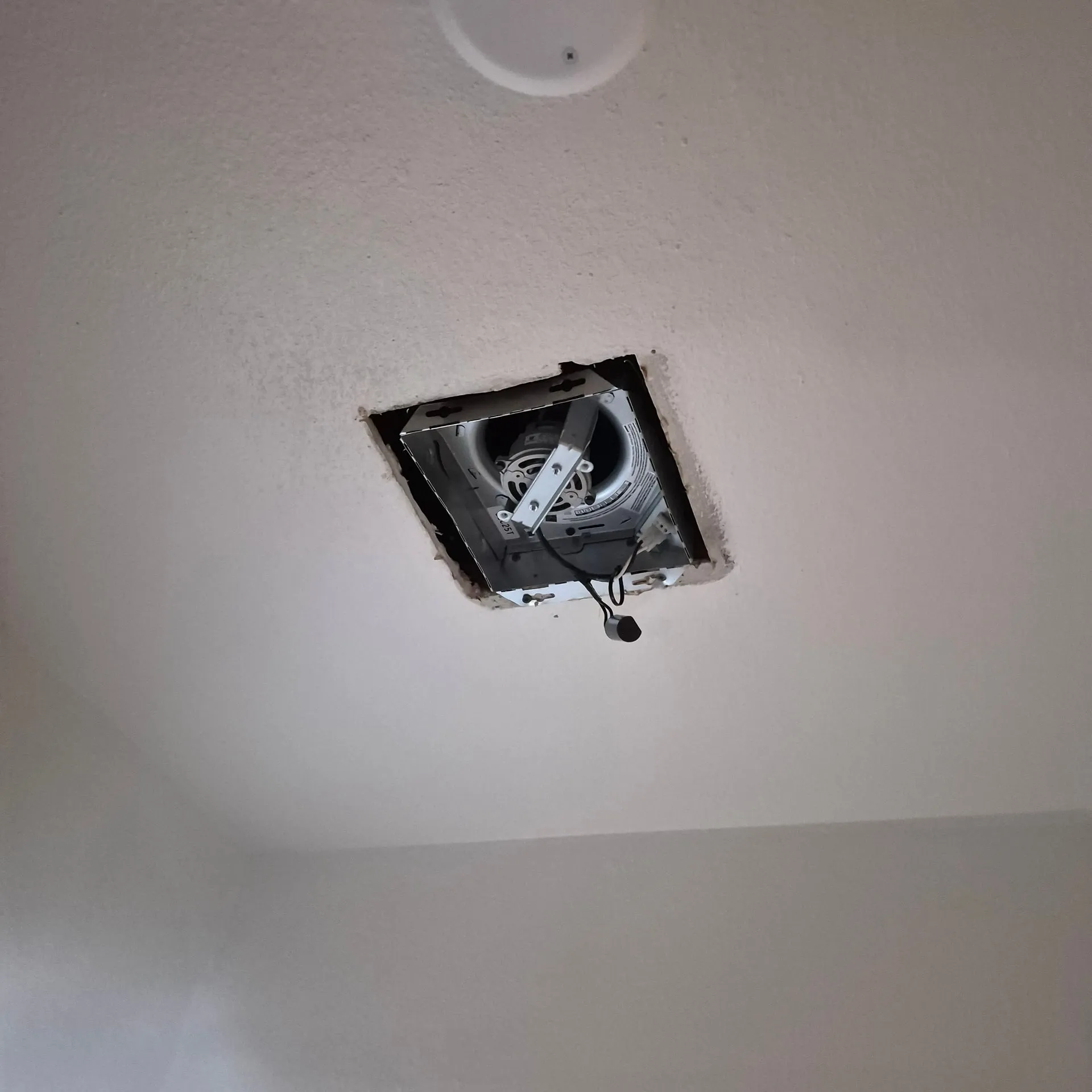 Bathroom exhaust fan housing in a Vancouver WA rental ceiling with the cover removed, the blower and wiring exposed, after the old fan was pulled and the circuit went dead