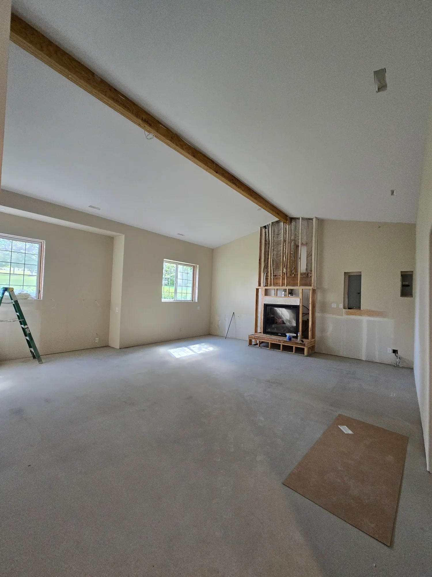 Vaulted Battle Ground WA great room with an exposed glulam ceiling beam, a framed fireplace surround, and newly installed recessed can lighting before flooring and finishes