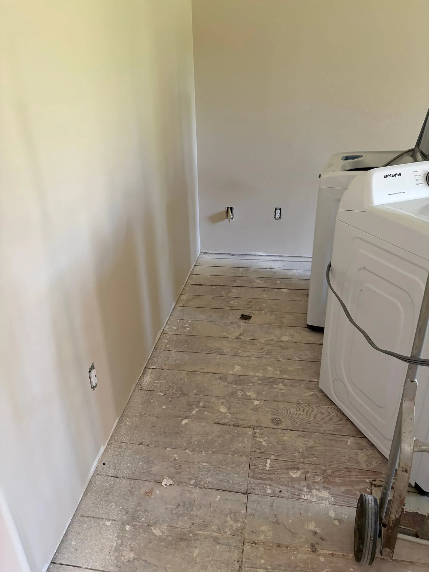Laundry room in a Vancouver WA home with the flooring removed to subfloor, open receptacle boxes on the wall, and a Samsung washer and dryer pushed aside for access