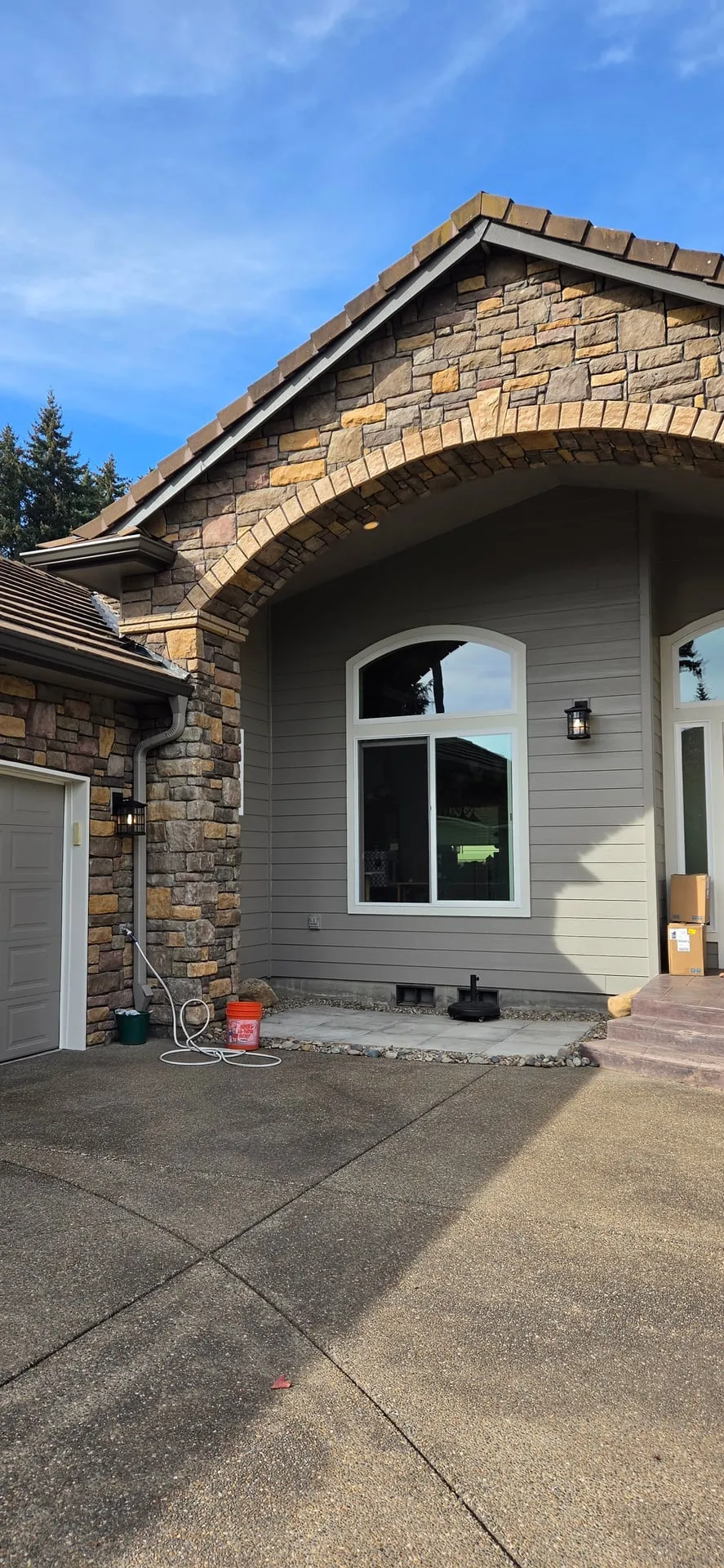 Front of an east Vancouver WA home with stone veneer and gray siding, showing new black wall lanterns beside the garage and at the front entry