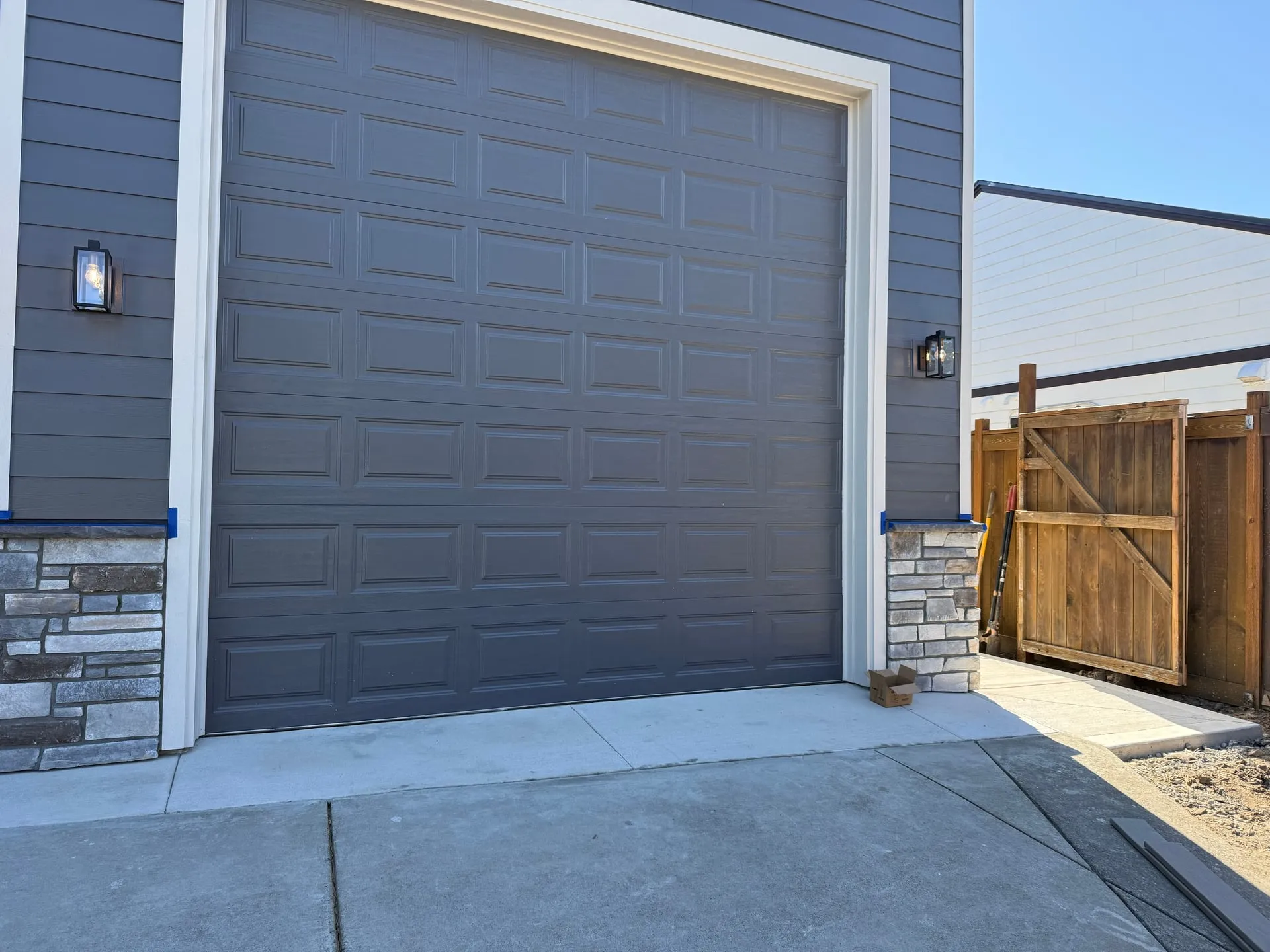 Exterior of a new shop building in Hazel Dell, Vancouver WA with a grey overhead garage door, stone base and coach lights mounted either side