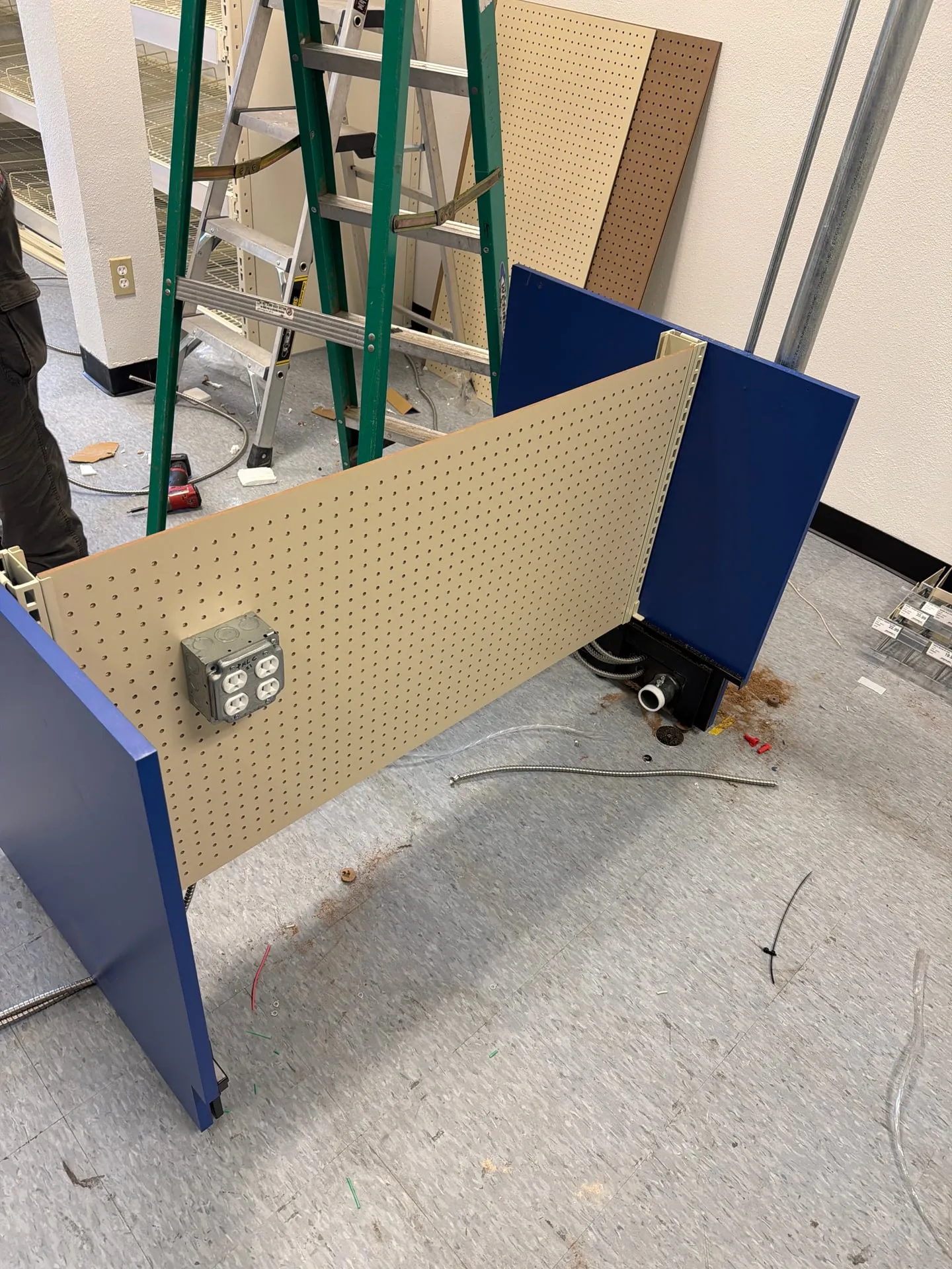 Store gondola end panel with a quad receptacle box and conduit running up to a ceiling power pole, with a ladder beside it