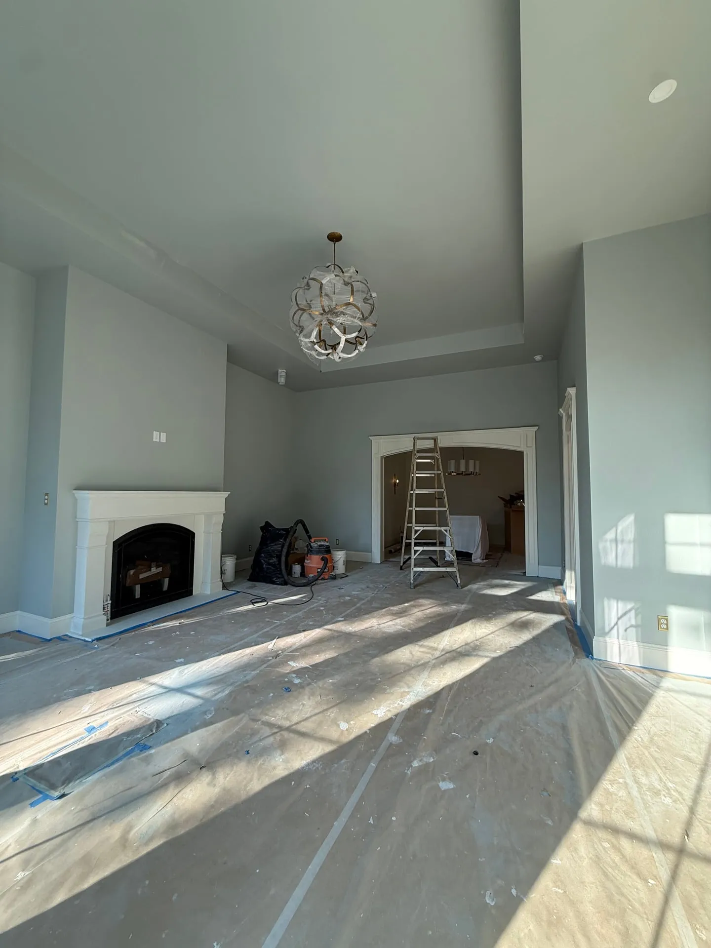 Great room of a custom home in Ridgefield WA during finishing, with a chandelier hung from the vaulted ceiling above a fireplace and floors still protected