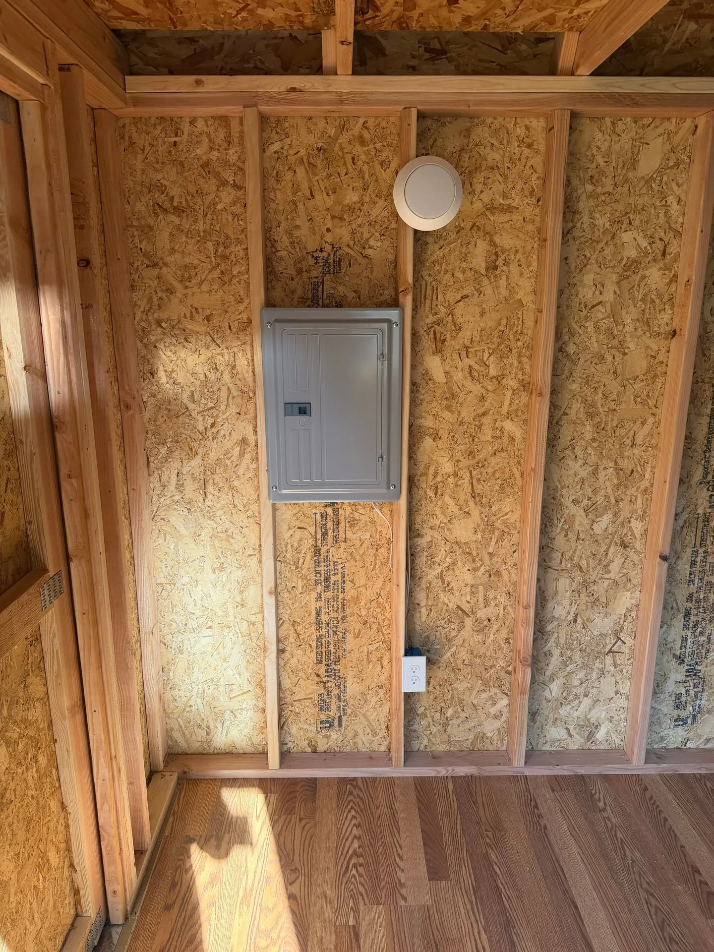 New 100-amp sub panel mounted on the OSB interior wall of a backyard shed in Woodland WA, with conduit entering the top of the enclosure and a finished wood floor below