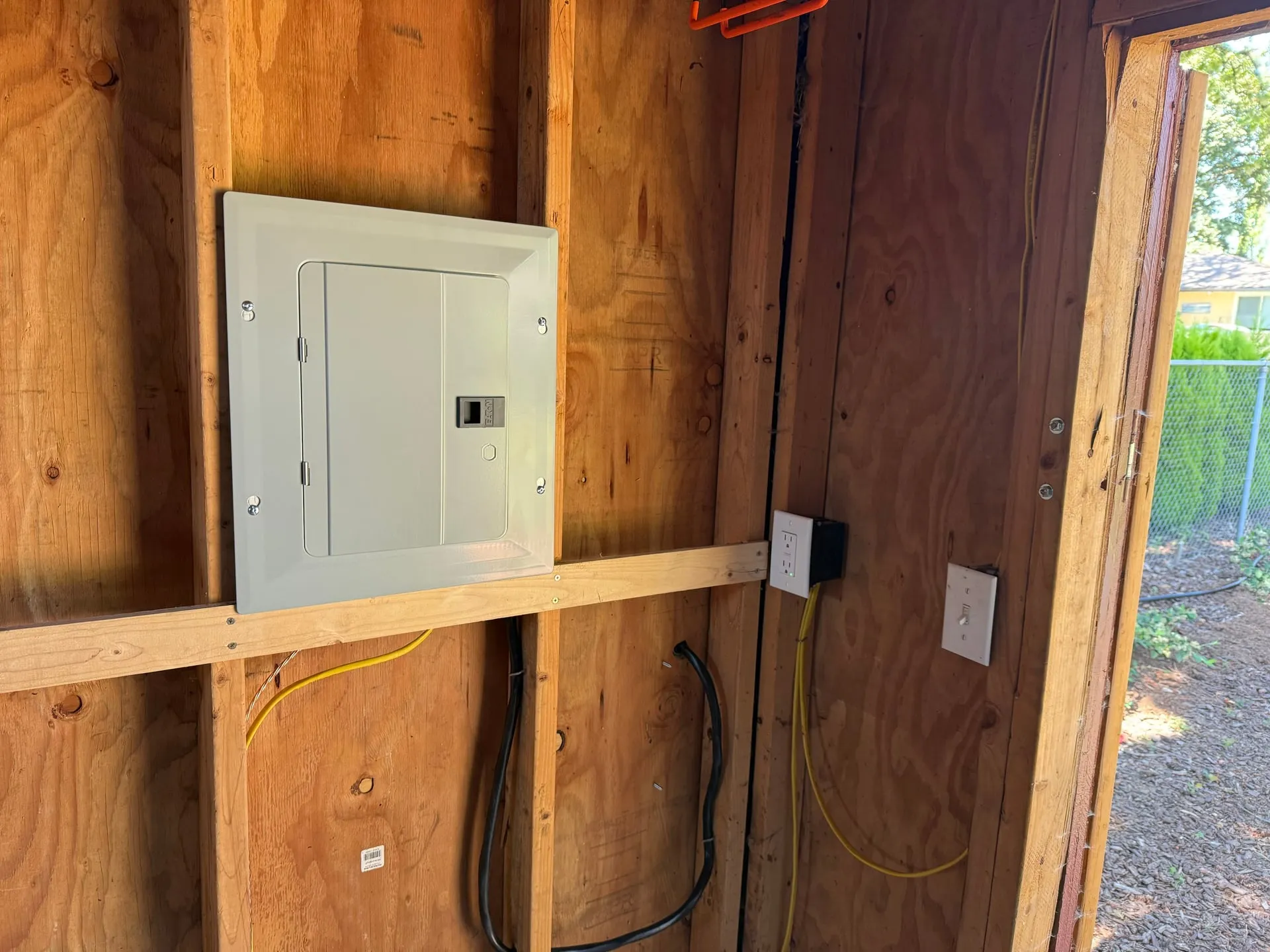 New 50-amp sub panel mounted on the plywood interior wall of a backyard shed in Vancouver WA, with conductors entering from below and a receptacle box beside the door opening
