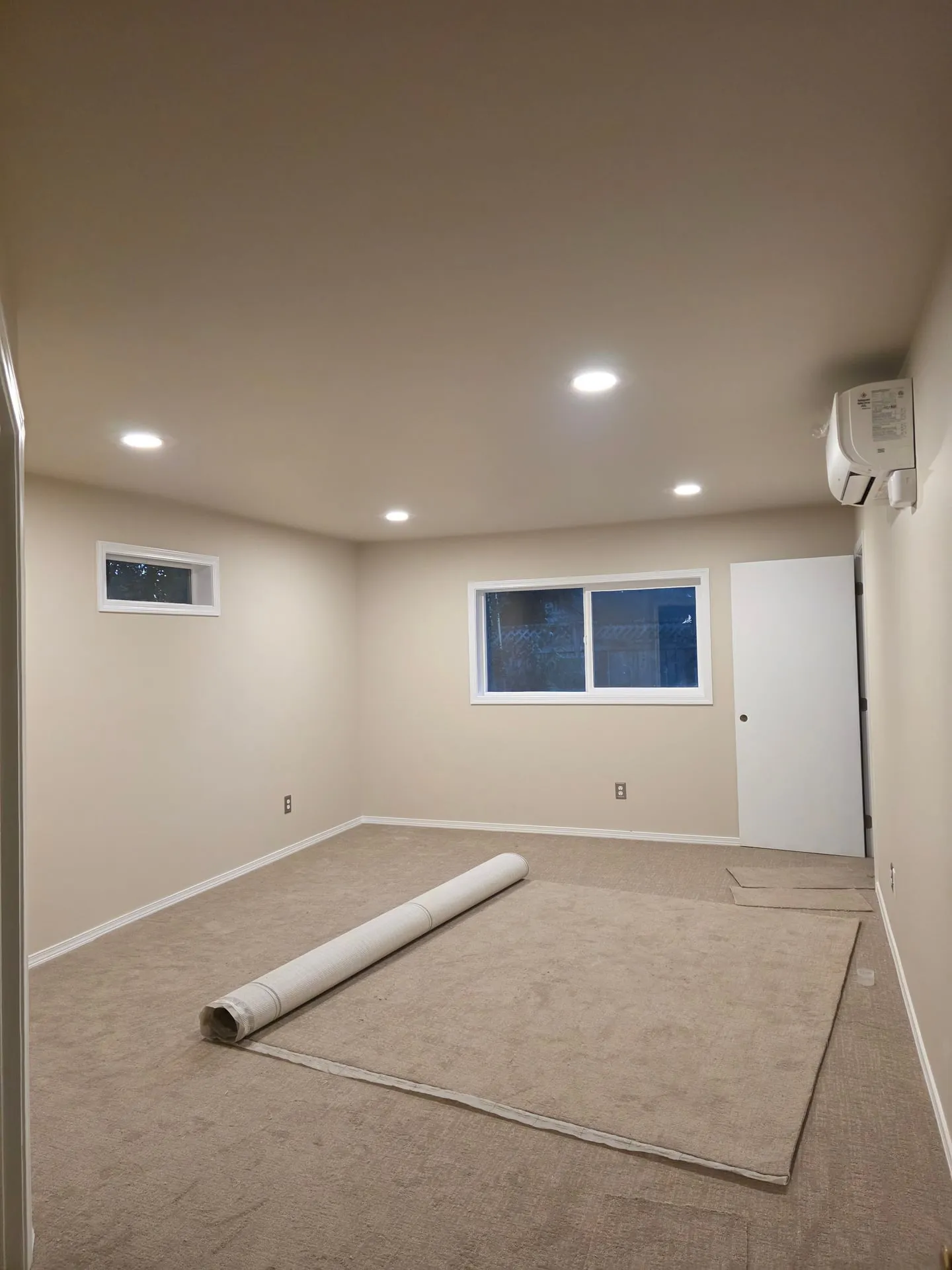 Finished bedroom addition in a Vancouver WA home with recessed lights on, a ductless mini split head on the wall and new carpet being laid