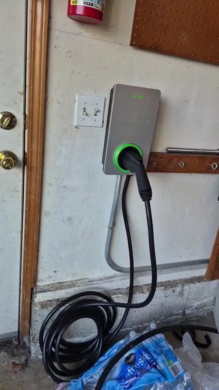 Wall-mounted Autel EV charger with an illuminated green status ring in a Vancouver WA garage, the connector holstered and the charging cable coiled below, fed by EMT conduit from the nearby panel