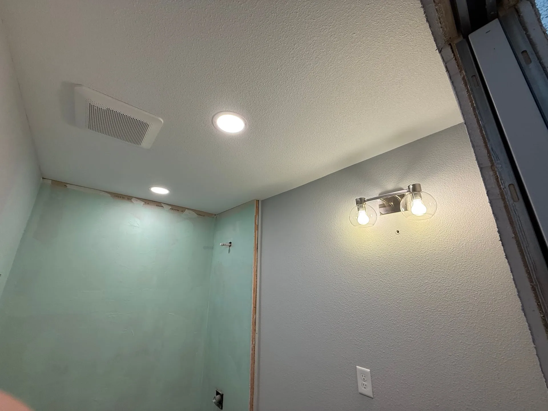 Remodeled bathroom in a Felida home in Vancouver WA at trim-out, with a Panasonic exhaust fan grille and 6-inch recessed can in the ceiling and a lit vanity light on the wall beside the window