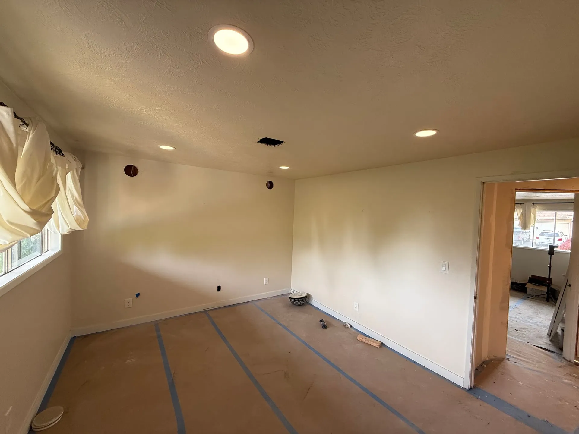 Bedroom in a Hazel Dell home in Vancouver WA with four new LED downlights lit in the ceiling, walls prepped and floors covered with protective paper and blue tape