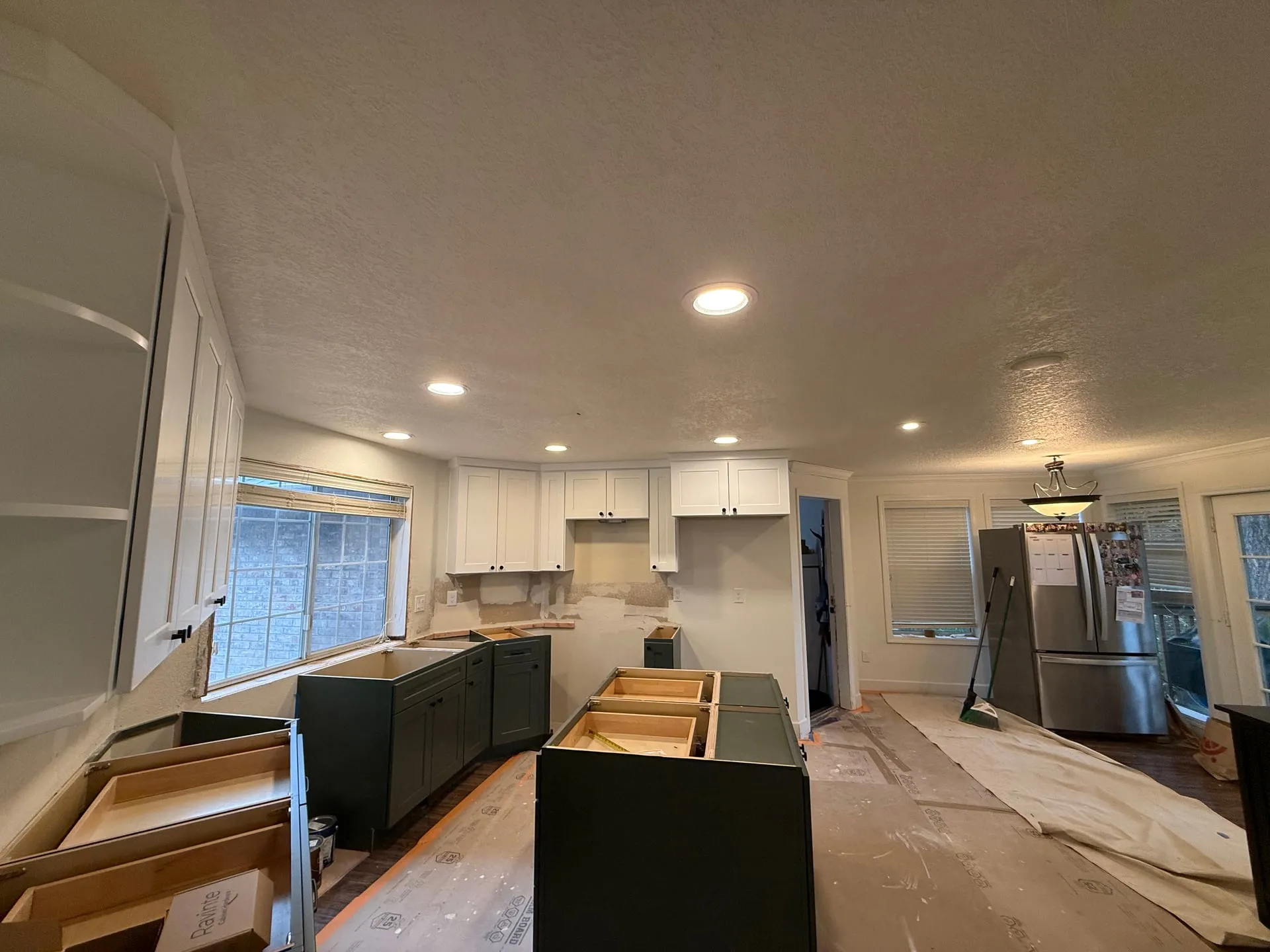 Vancouver WA kitchen and adjoining room lit by newly installed canless LED downlights, with dark green base cabinets, white uppers and the ceiling free of the old dropped soffit