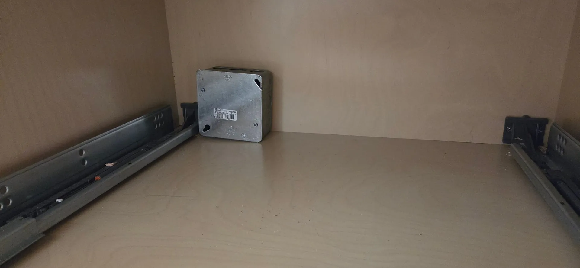 Covered steel junction box sitting at the back of an empty drawer base cabinet with drawer slides on both sides in a Ridgefield WA kitchen