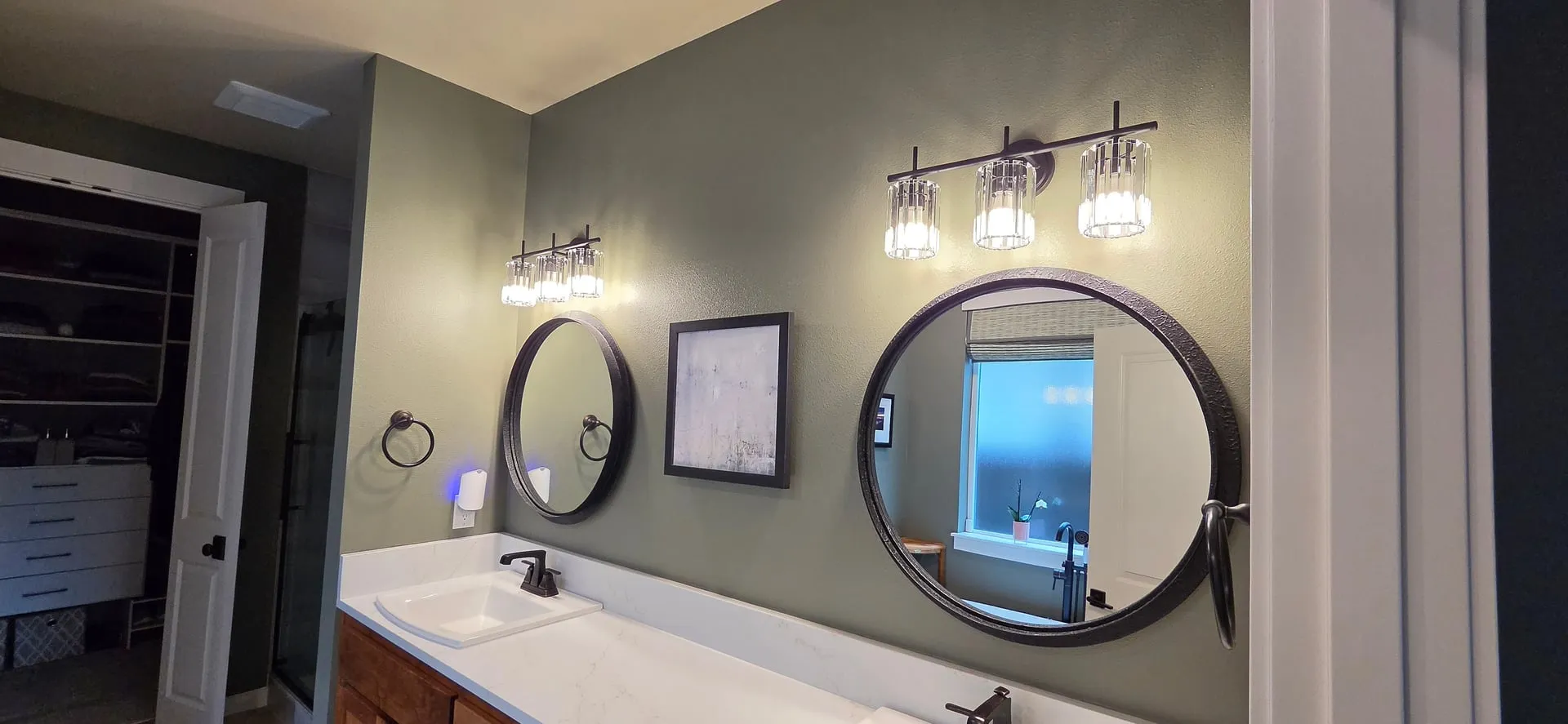 Two new three-light crystal vanity fixtures over round black-framed mirrors and a white quartz double vanity in a Vancouver WA bathroom with sage green walls