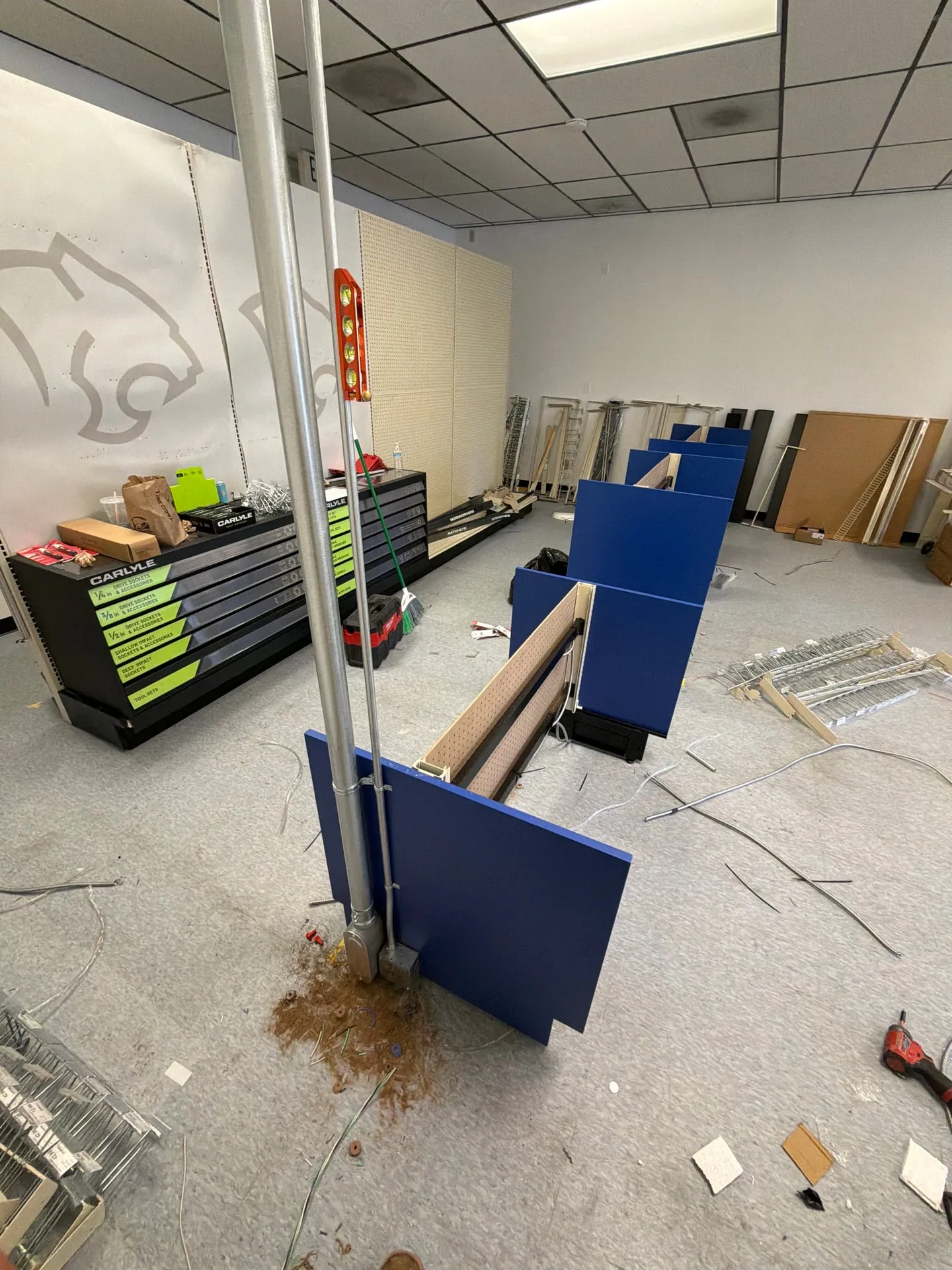 EMT conduit power pole dropping from a drop ceiling to a new blue and tan pegboard gondola on the sales floor of a retail store buildout in Vancouver WA, with tool cabinets and shelving parts around it