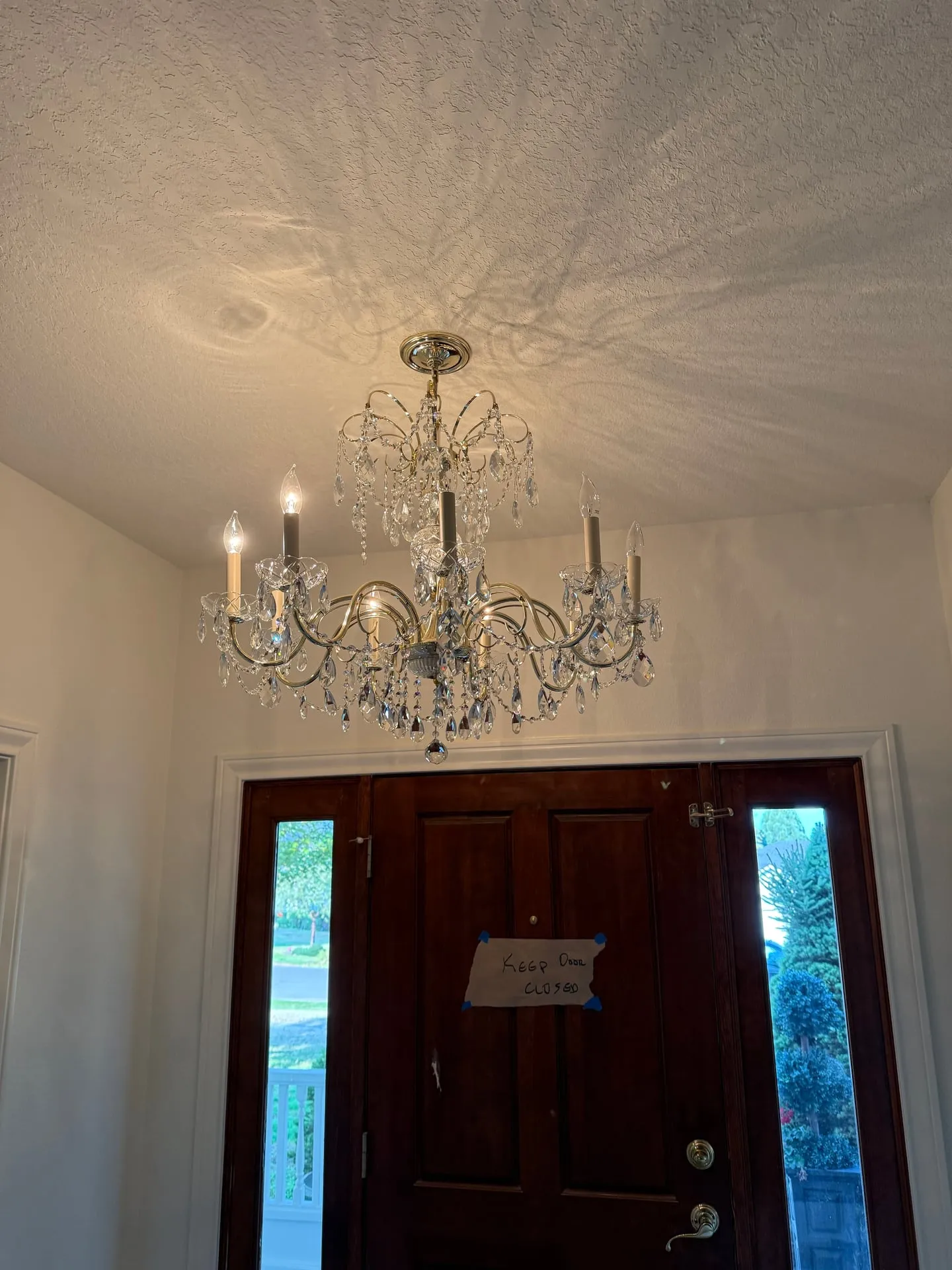 Crystal chandelier hanging above the entry hall of a custom home in Ridgefield WA, with a dark stained front door, white panelled walls and a swirled plaster ceiling above
