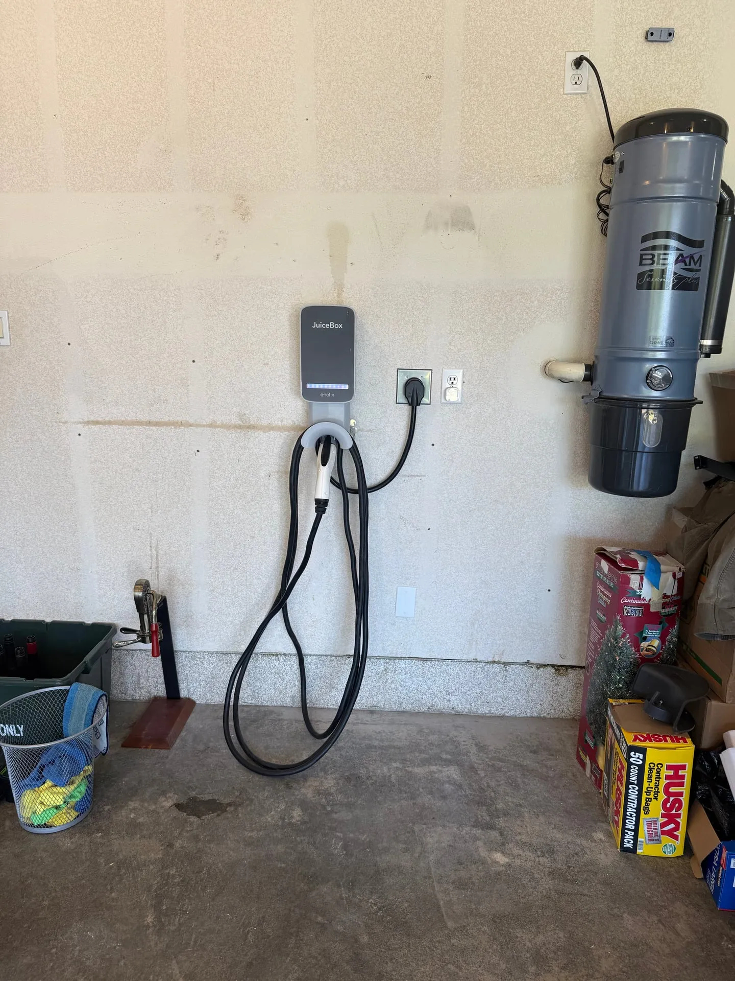 Wall-mounted EV charger installed on the garage wall of a Vancouver WA home with its cable coiled on the holster, next to a central vacuum canister