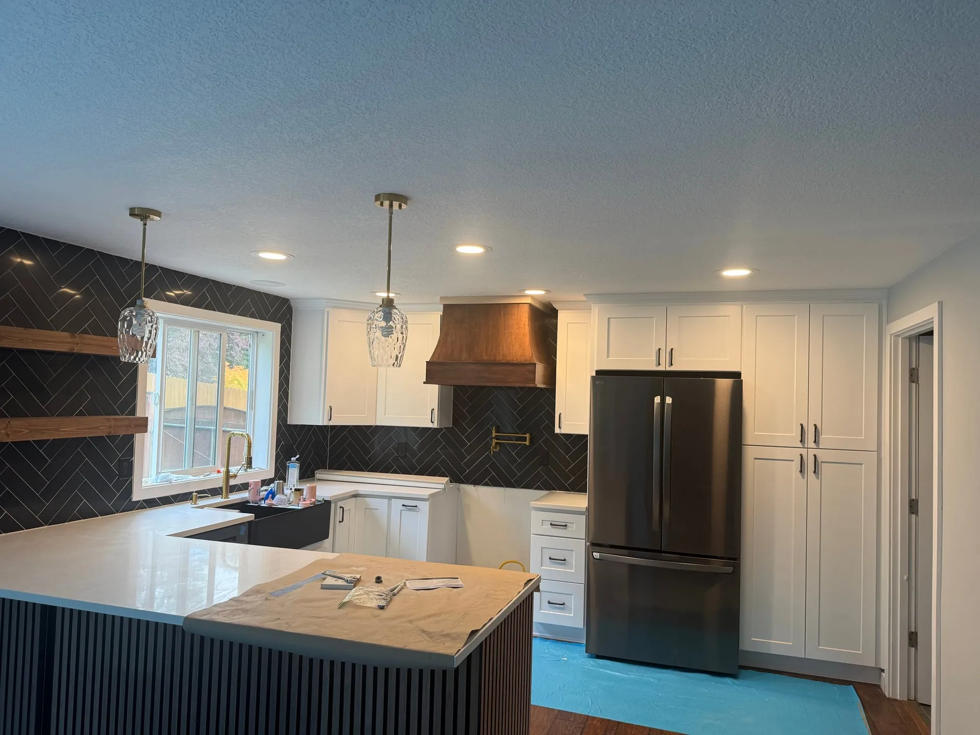Remodeled kitchen in Washougal WA with white shaker cabinets, a wood range hood, a black herringbone tile backsplash, recessed lighting, a glass pendant over the island and a dark stainless refrigerator