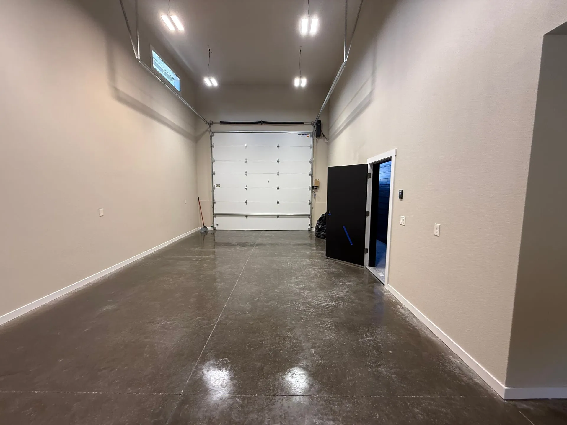 Shop bay of a new 1,062 square foot outbuilding in Hazel Dell, Vancouver WA, lit by a row of high bay LED fixtures down the ceiling with polished concrete floor and the overhead door at the far end