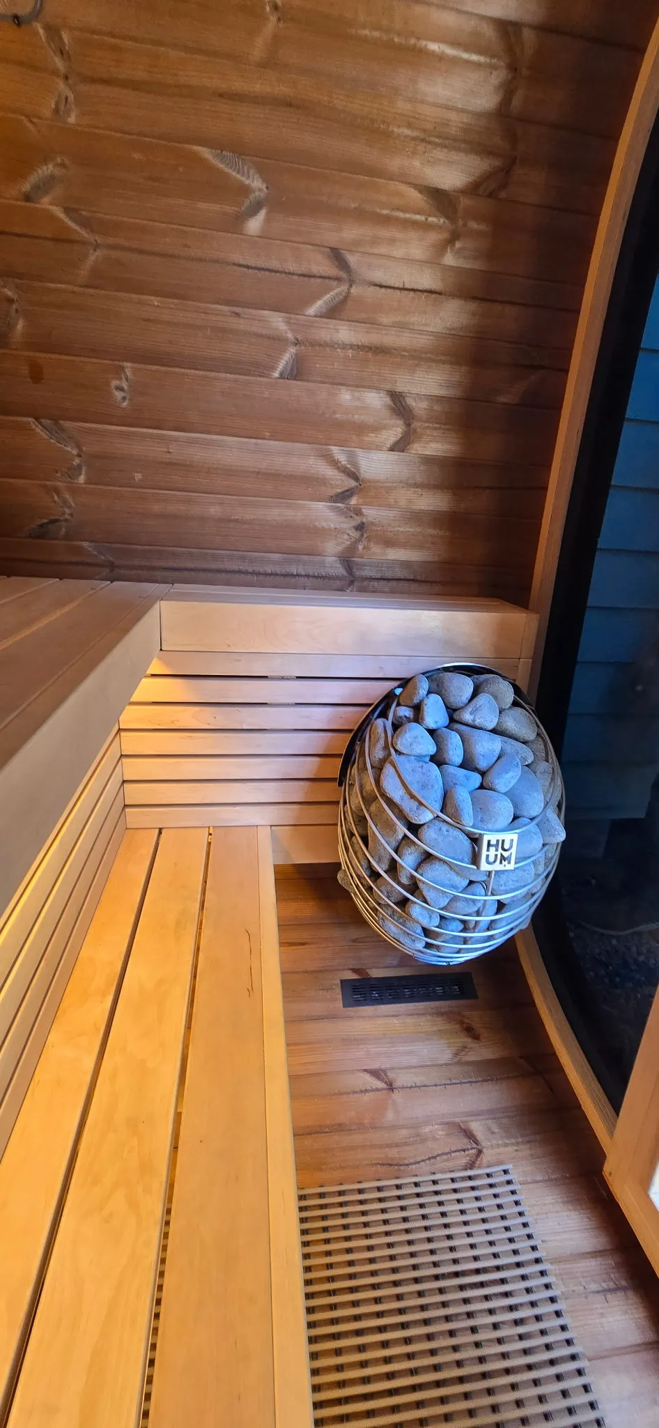 Huum Drop electric sauna heater with its stone-filled cylindrical body installed inside a cedar-lined outdoor sauna in Washougal WA, with LED strip lighting glowing under the bench