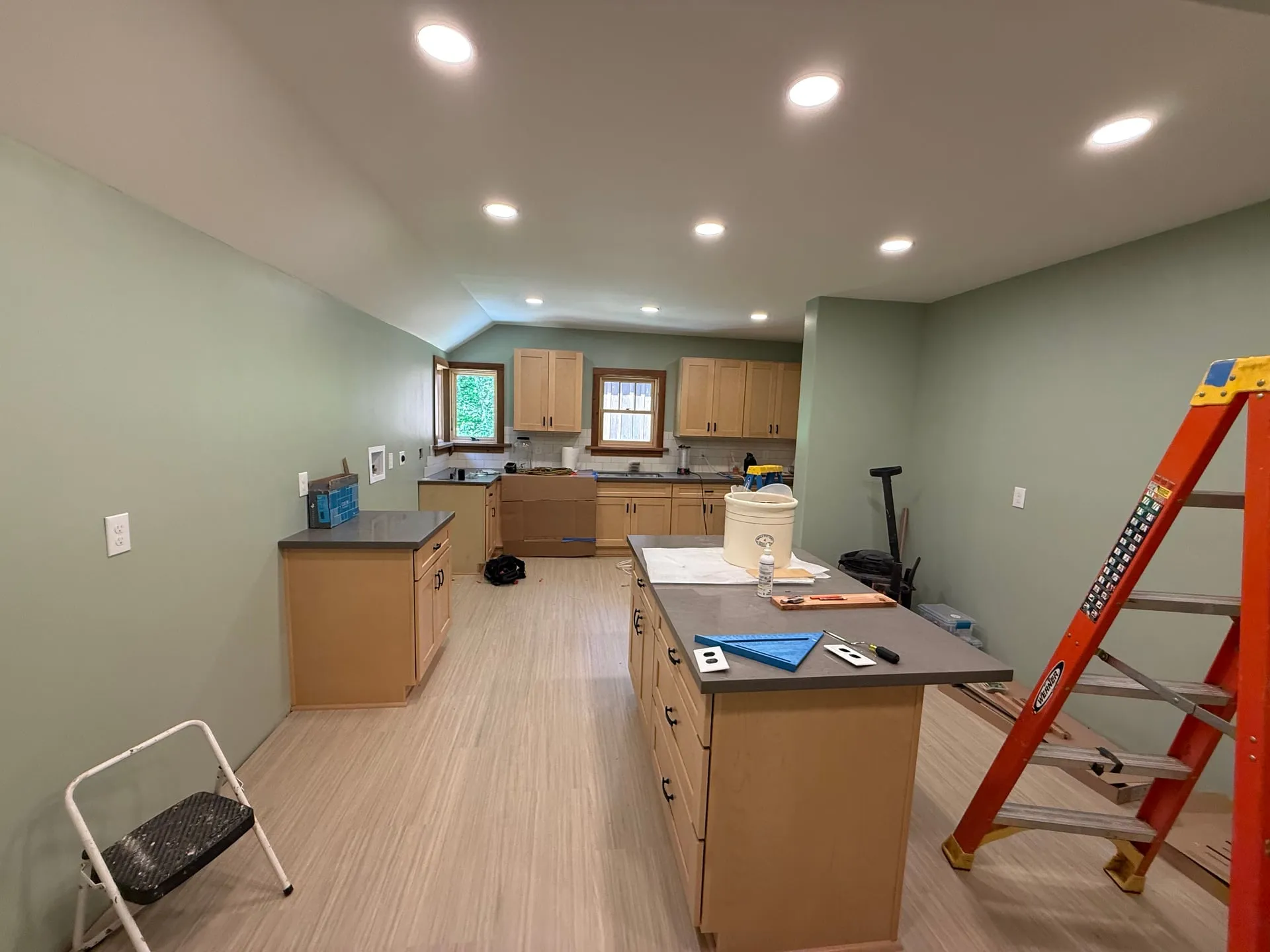 Remodeled kitchen in a Yacolt WA home at trim-out with recessed can lighting across the ceiling, a centre island, light wood cabinets and pale flooring, with a ladder still in the room