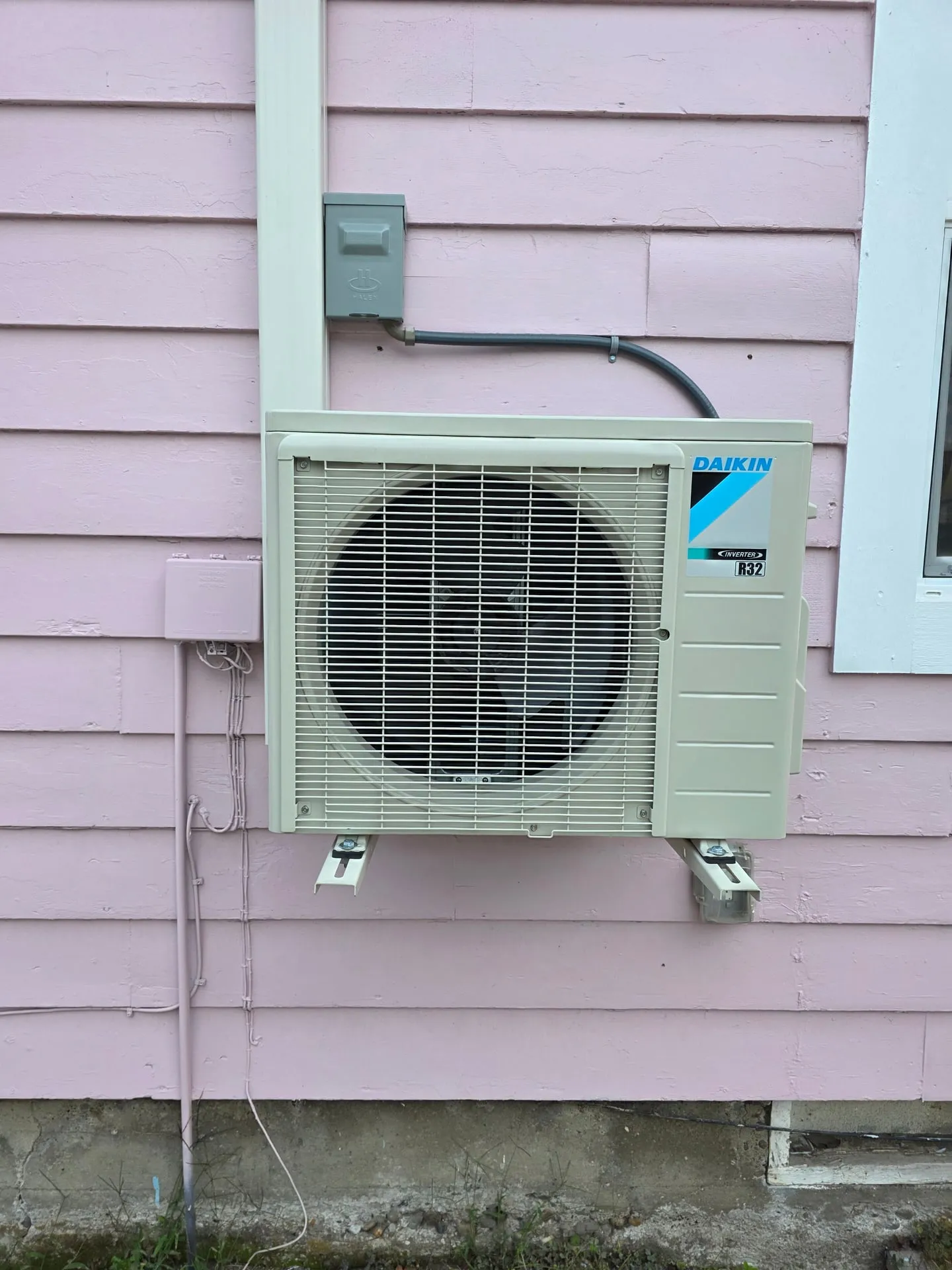 Daikin mini split outdoor unit on wall brackets with a gray disconnect box above it on pink siding at a Woodland WA home