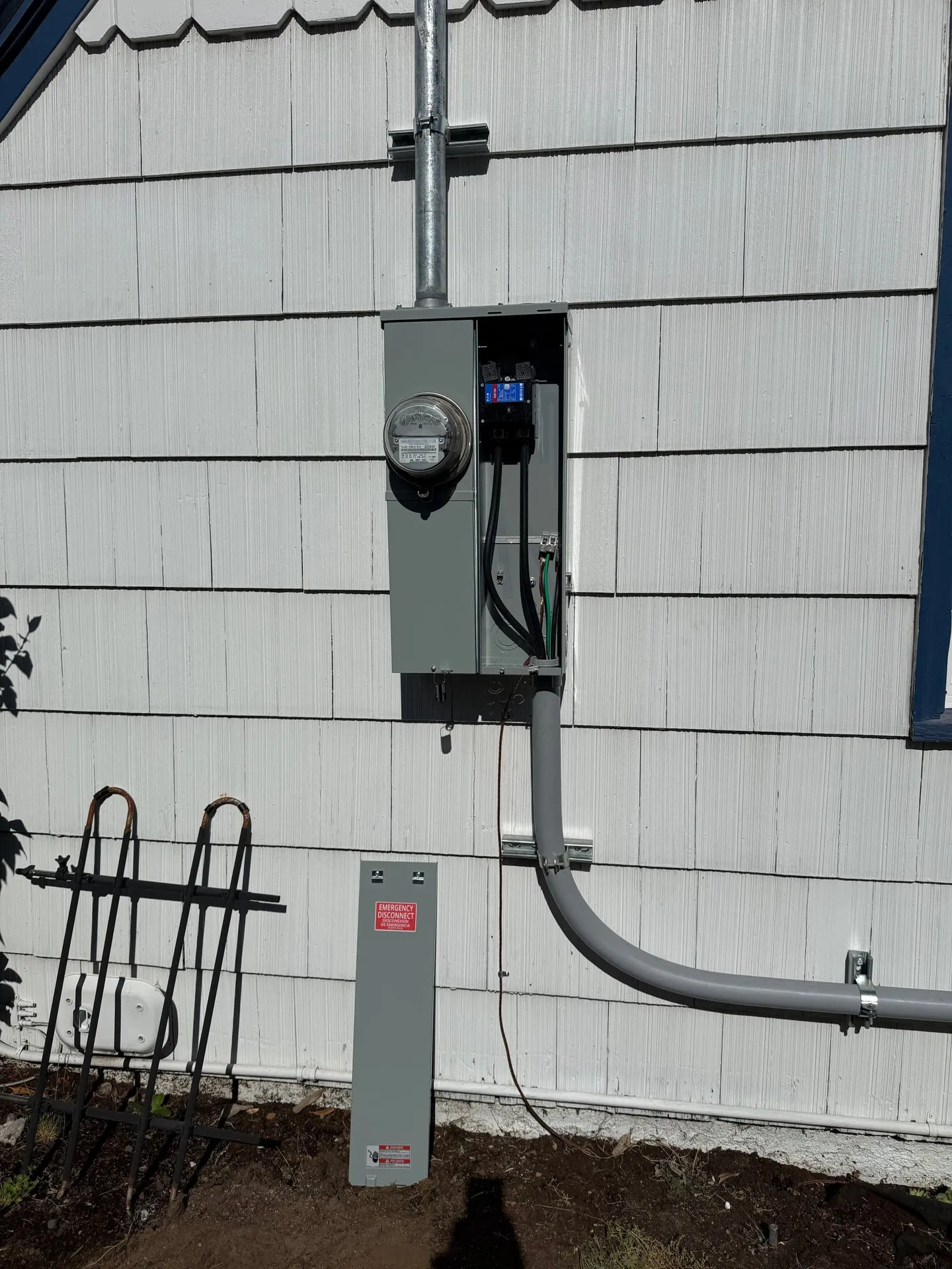 New 200-amp meter main installed on the white shingle siding of an older Vancouver WA home, with galvanized mast above and conduit running down to a pedestal enclosure at grade