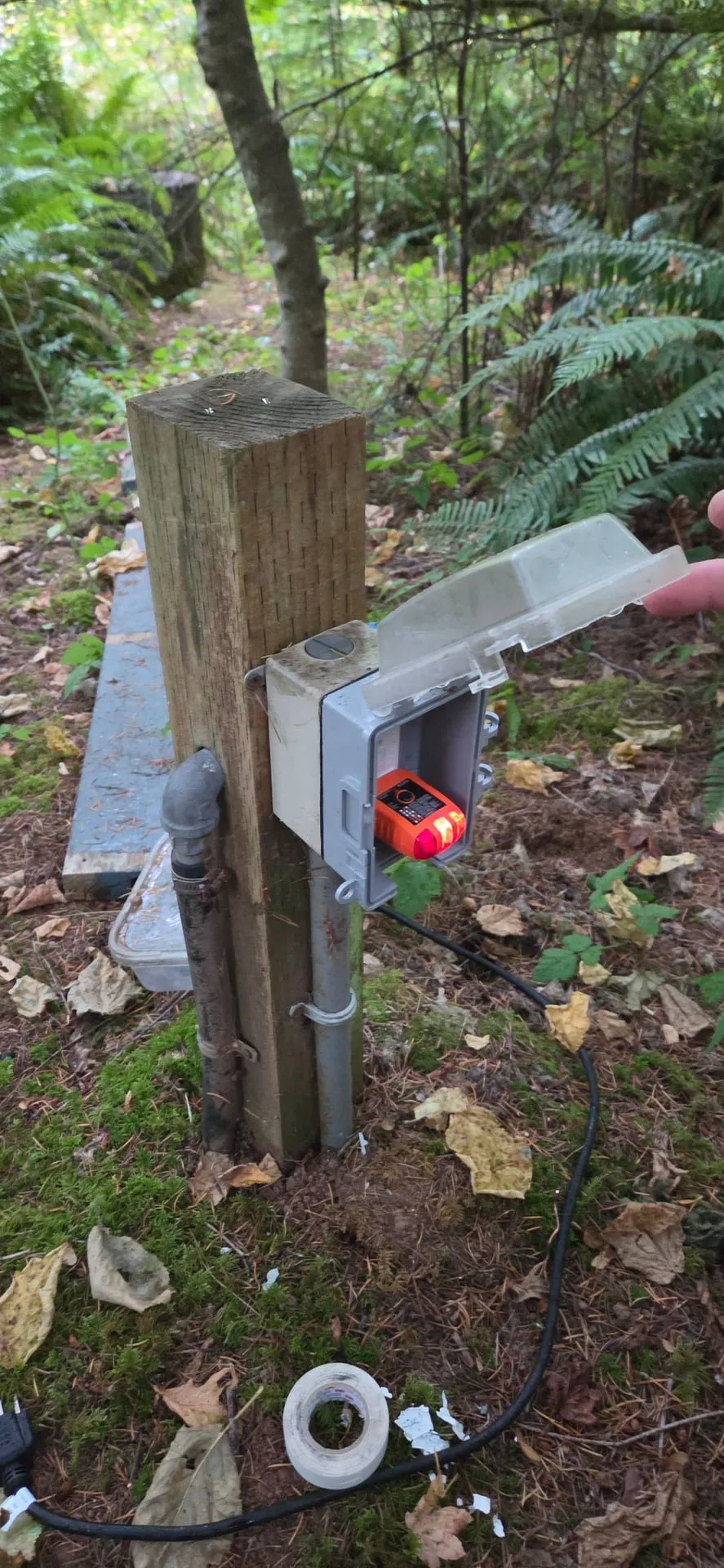 New outdoor GFCI outlet with a clear in-use cover mounted on a wood post in a garden on a Camas WA property