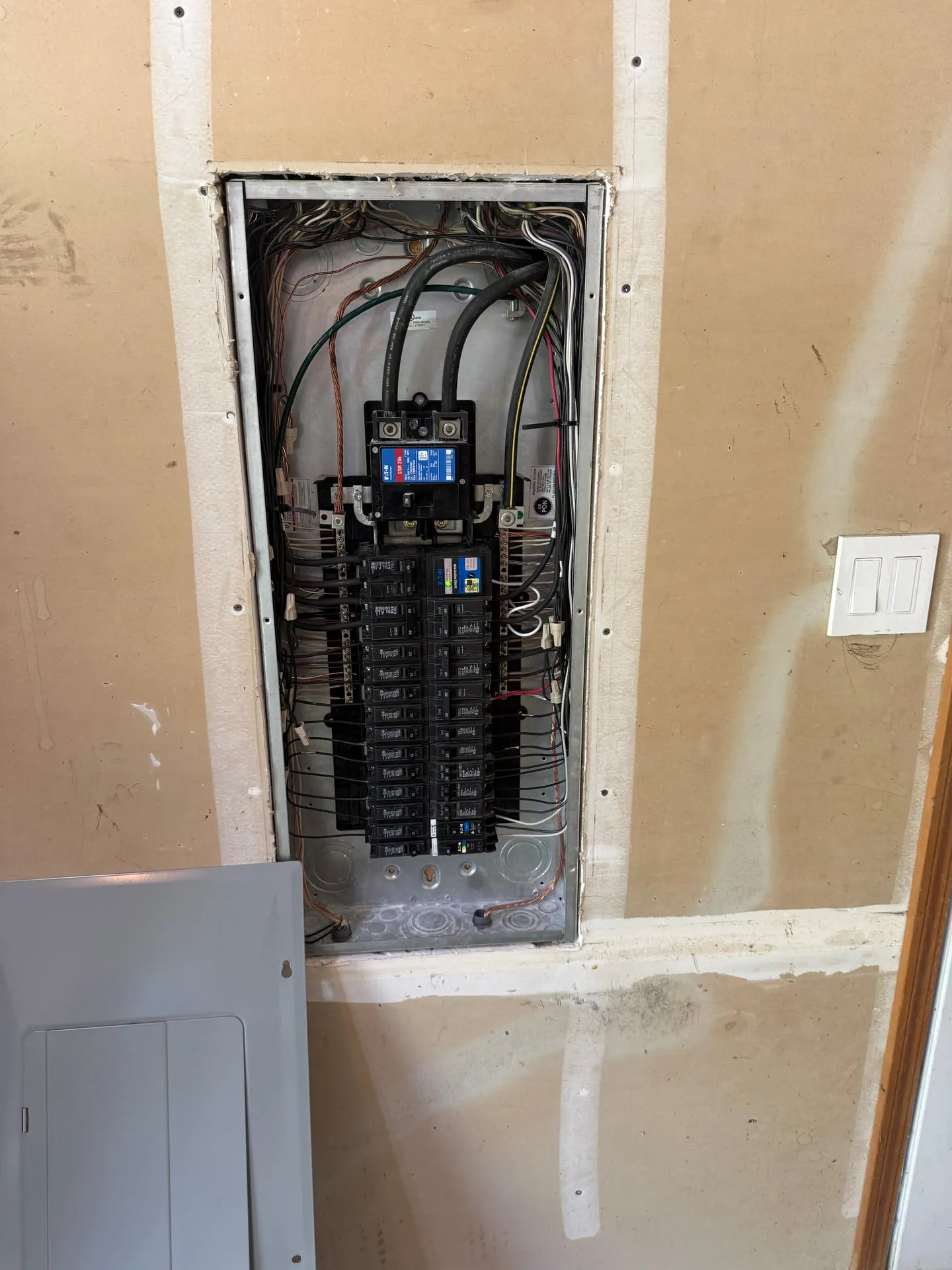 New electrical panel installed in a Kalama WA garage with the dead front removed, showing a surge protective device at the top of the bus and branch circuit conductors landed around it