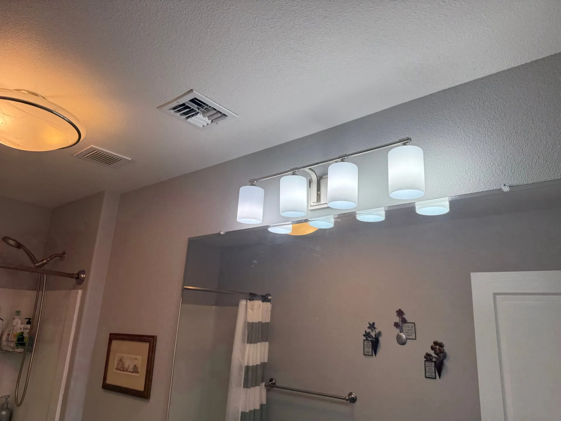 Bathroom in a Ridgefield WA home with a new five-light vanity fixture lit above the mirror, a flush ceiling light and a shower with grab bars visible beyond