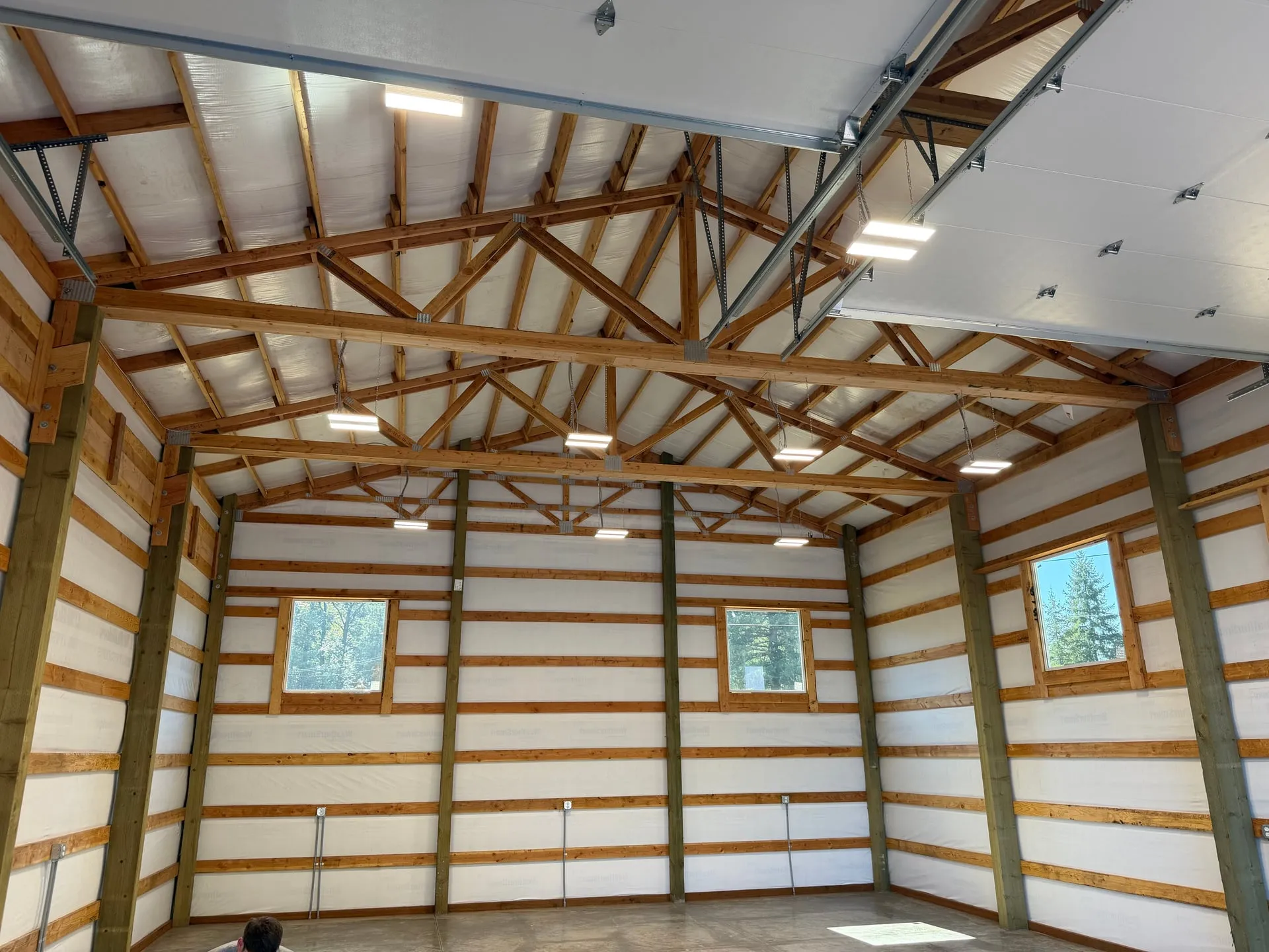 Interior of a new pole barn in Battle Ground WA with LED strip lighting mounted between the exposed trusses, white steel liner panels and a polished concrete floor