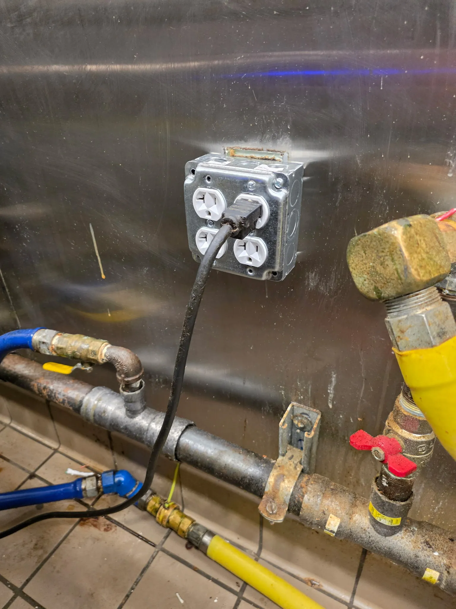 New quad outlet in a metal box on a stainless steel wall behind a restaurant cook line in Ridgefield WA, next to gas lines and a water hose