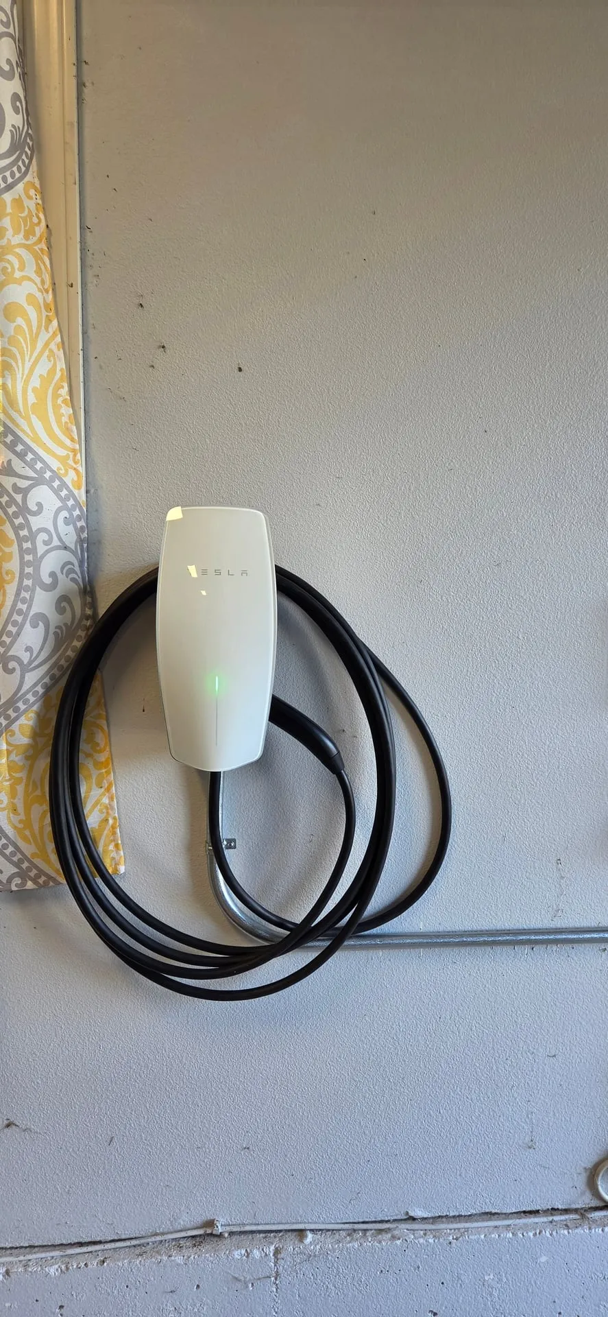 White Tesla Wall Connector with its cable coiled, mounted on a painted concrete garage wall in Camas WA with conduit running along the wall