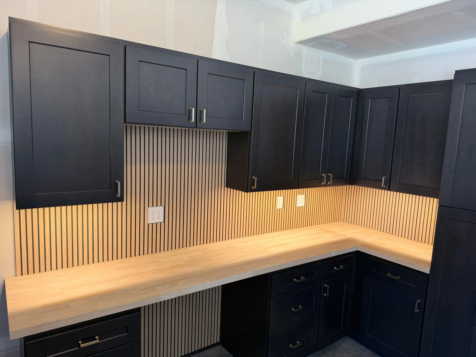 Under-cabinet lighting washing down a white oak counter and fluted wood backsplash beneath navy shaker cabinets in an Orchards home in Vancouver WA