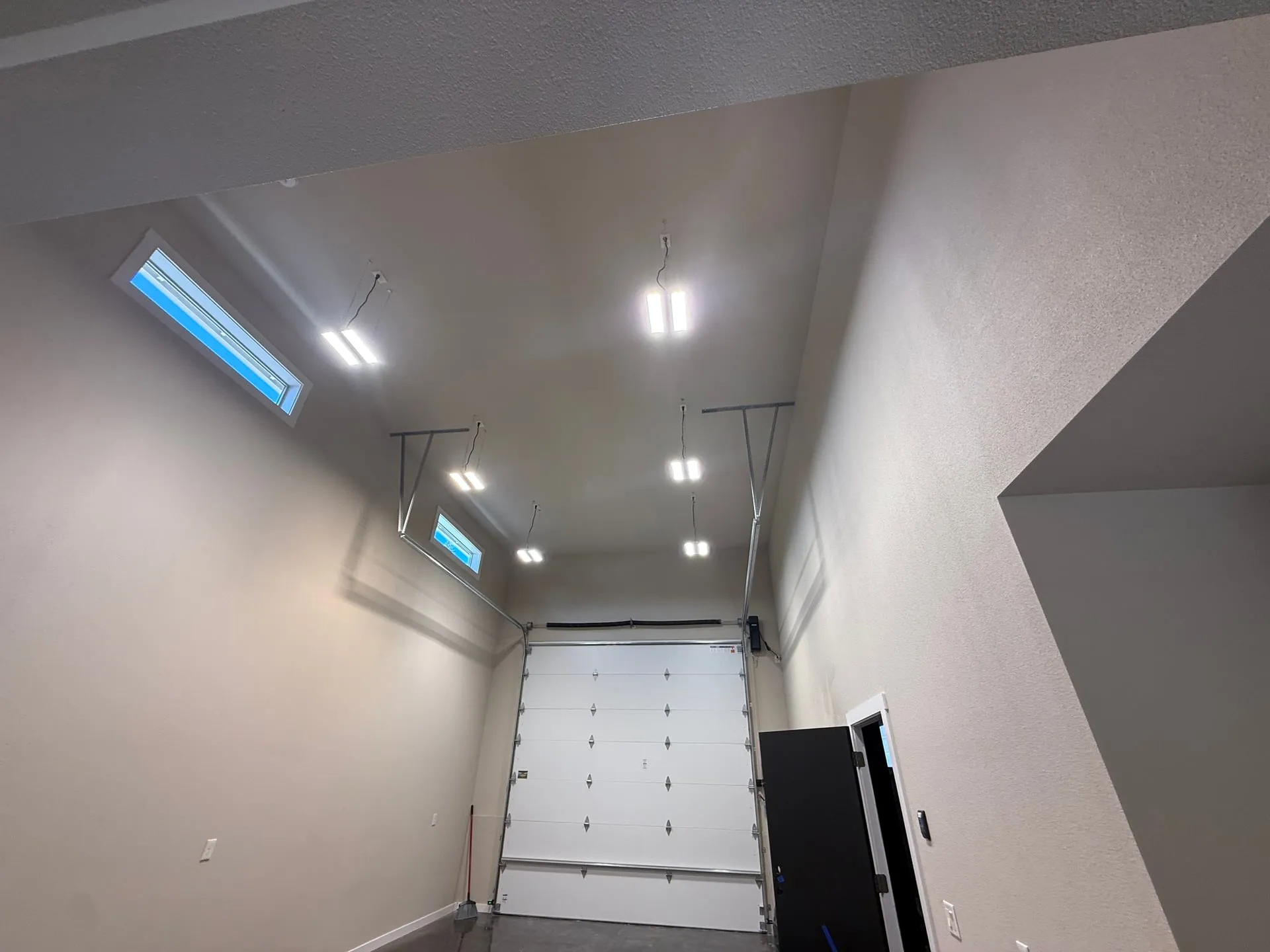 High bay LED fixtures suspended over the shop bay of a new outbuilding in Hazel Dell, Vancouver WA, with skylights along the ridge and the overhead door open at the end