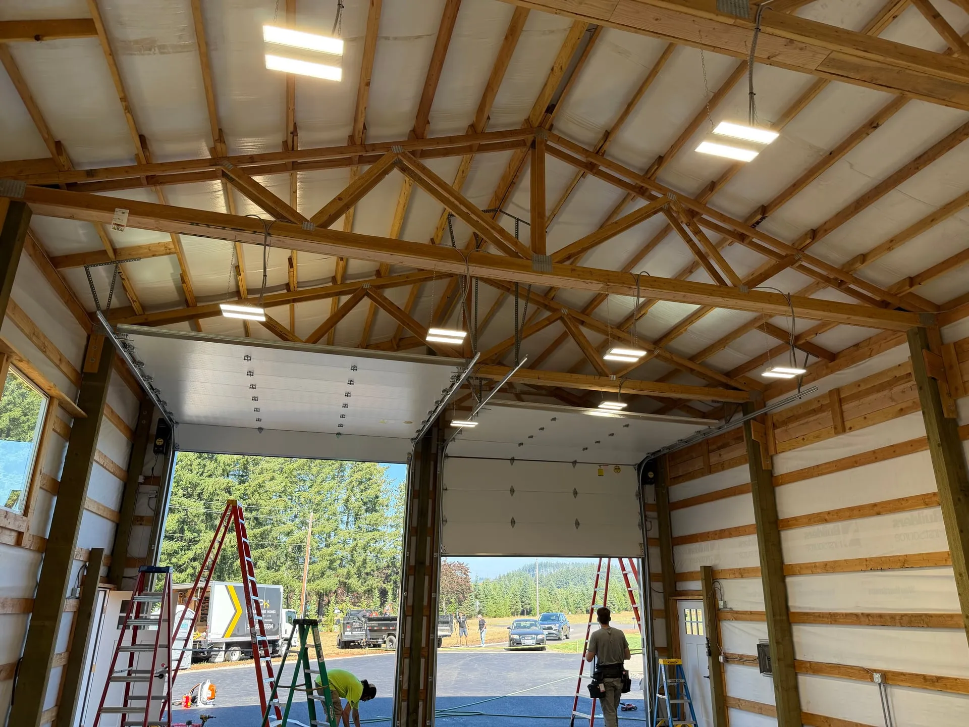Interior of a new pole barn in Battle Ground WA seen through the open overhead door, with LED lighting running the length of the trusses