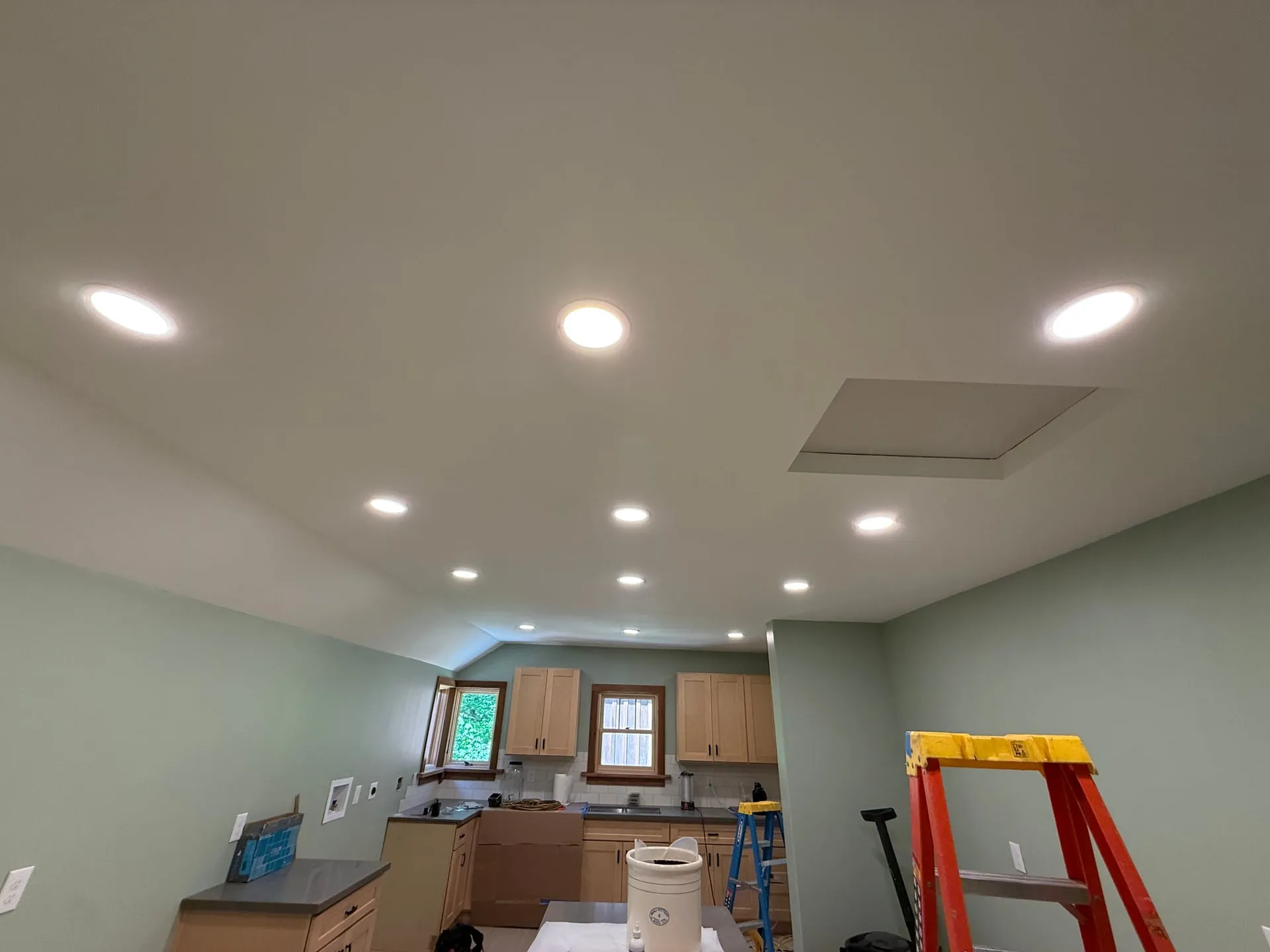 Remodeled Yacolt WA kitchen seen from the dining side at trim-out, with recessed cans lit across the ceiling and a range hood opening above the counter run
